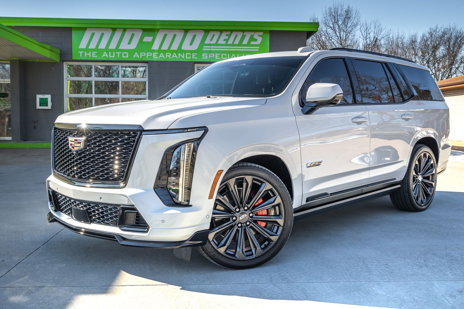 White Cadillac Escalade SUV parked outside a business with a green sign that says