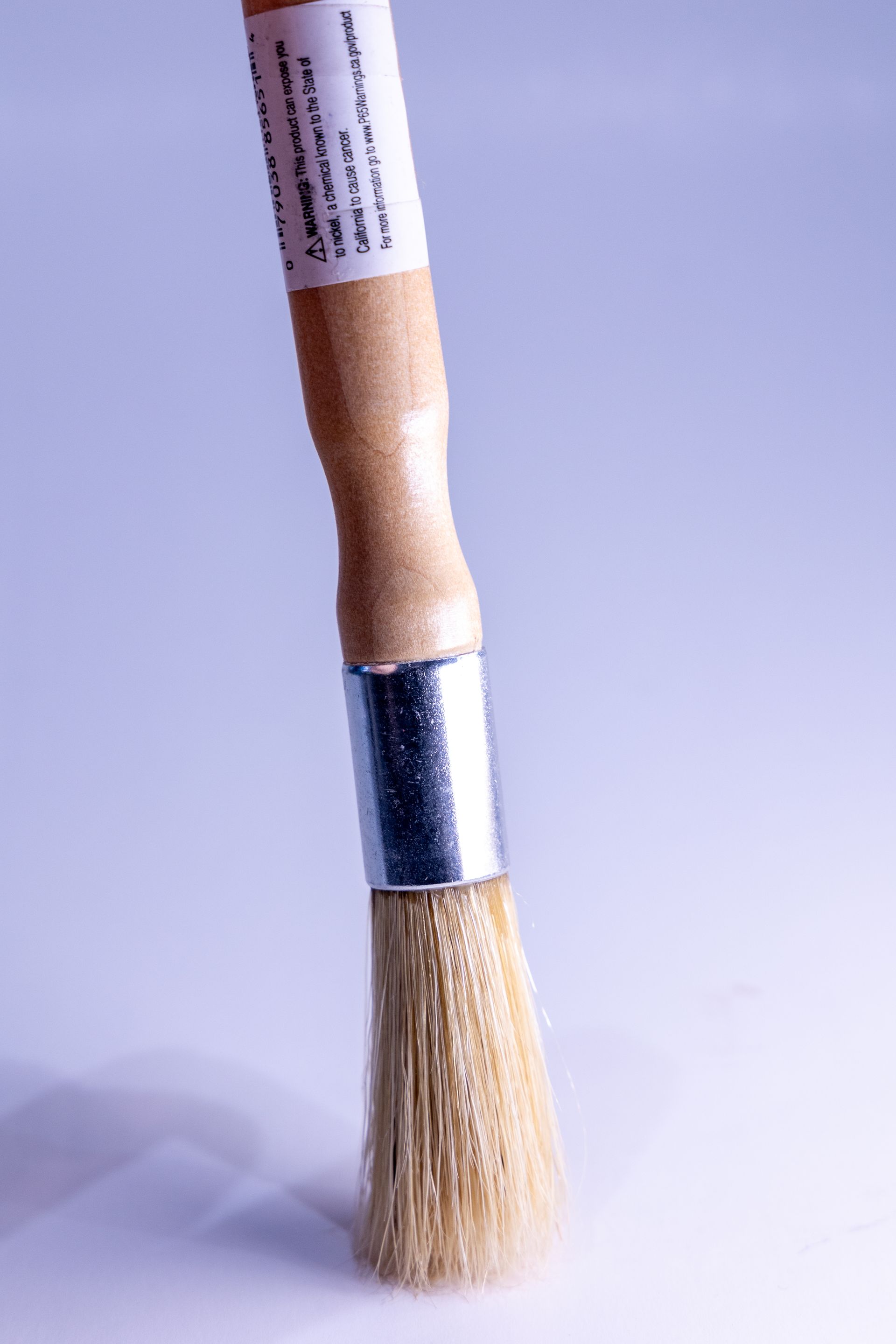 A small brush with a wooden handle is sitting on a white surface.
