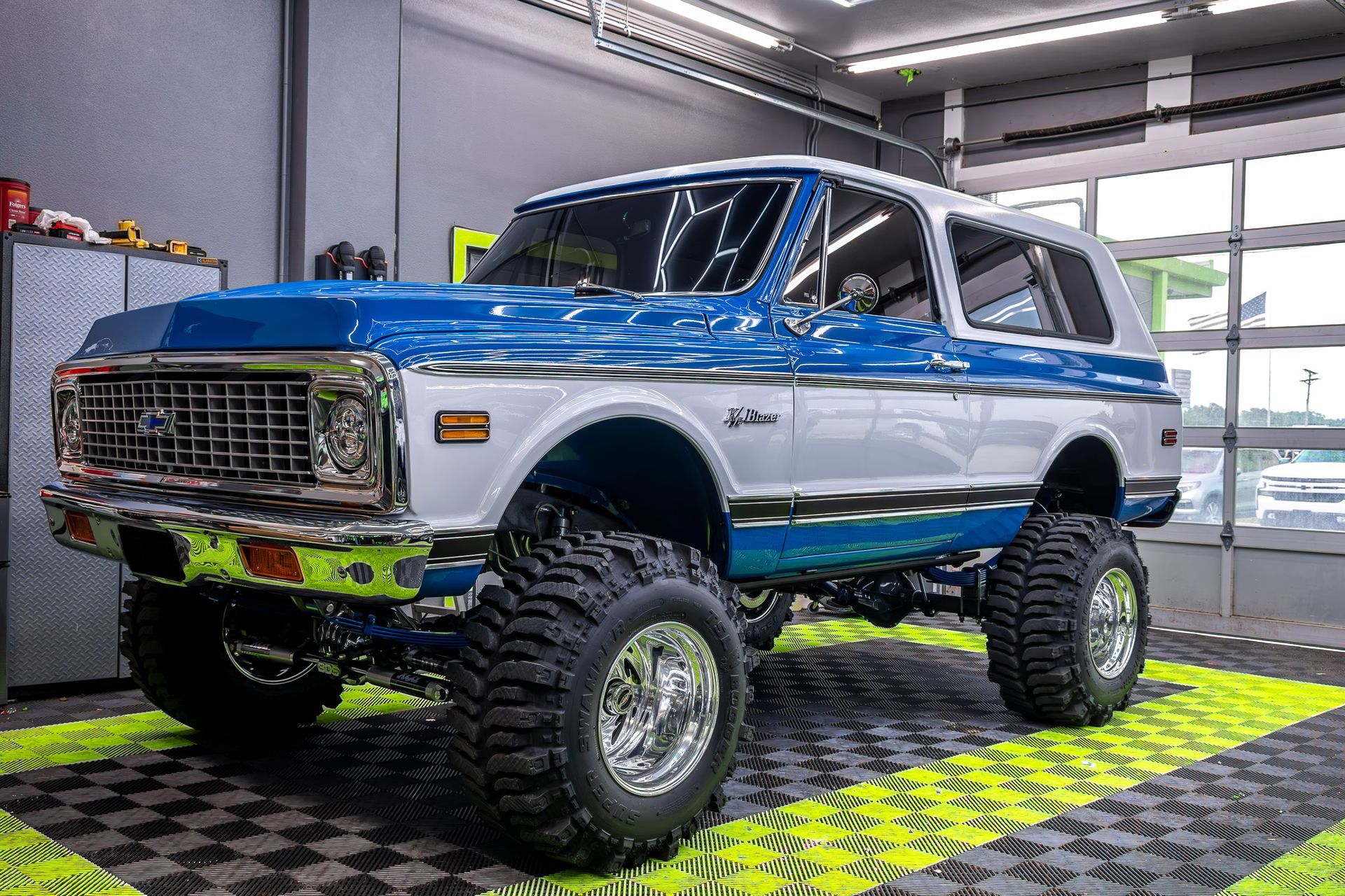 Blue and white lifted Chevrolet Blazer on chrome wheels in a garage.