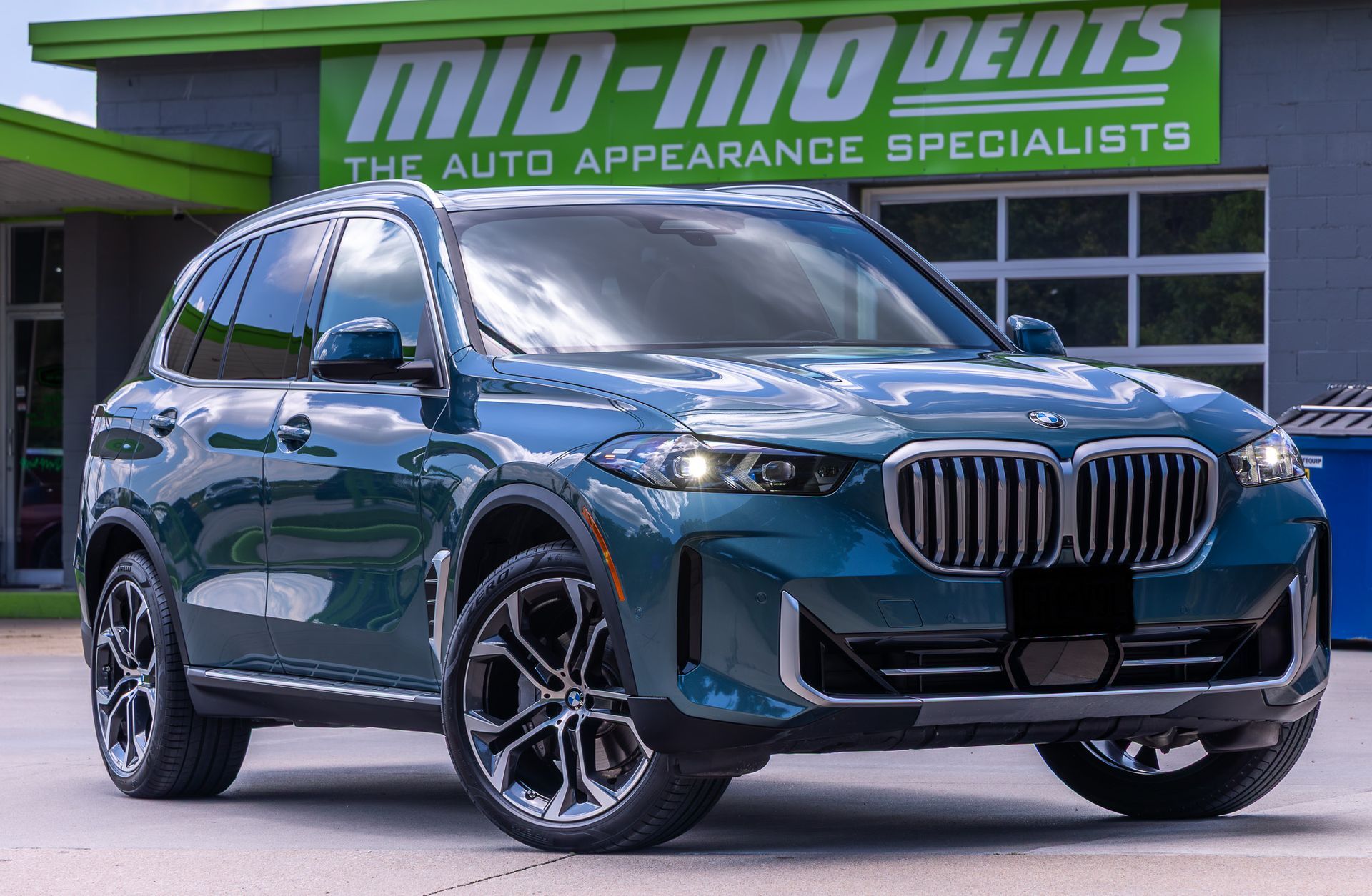 Blue BMW SUV parked in front of a car appearance shop.