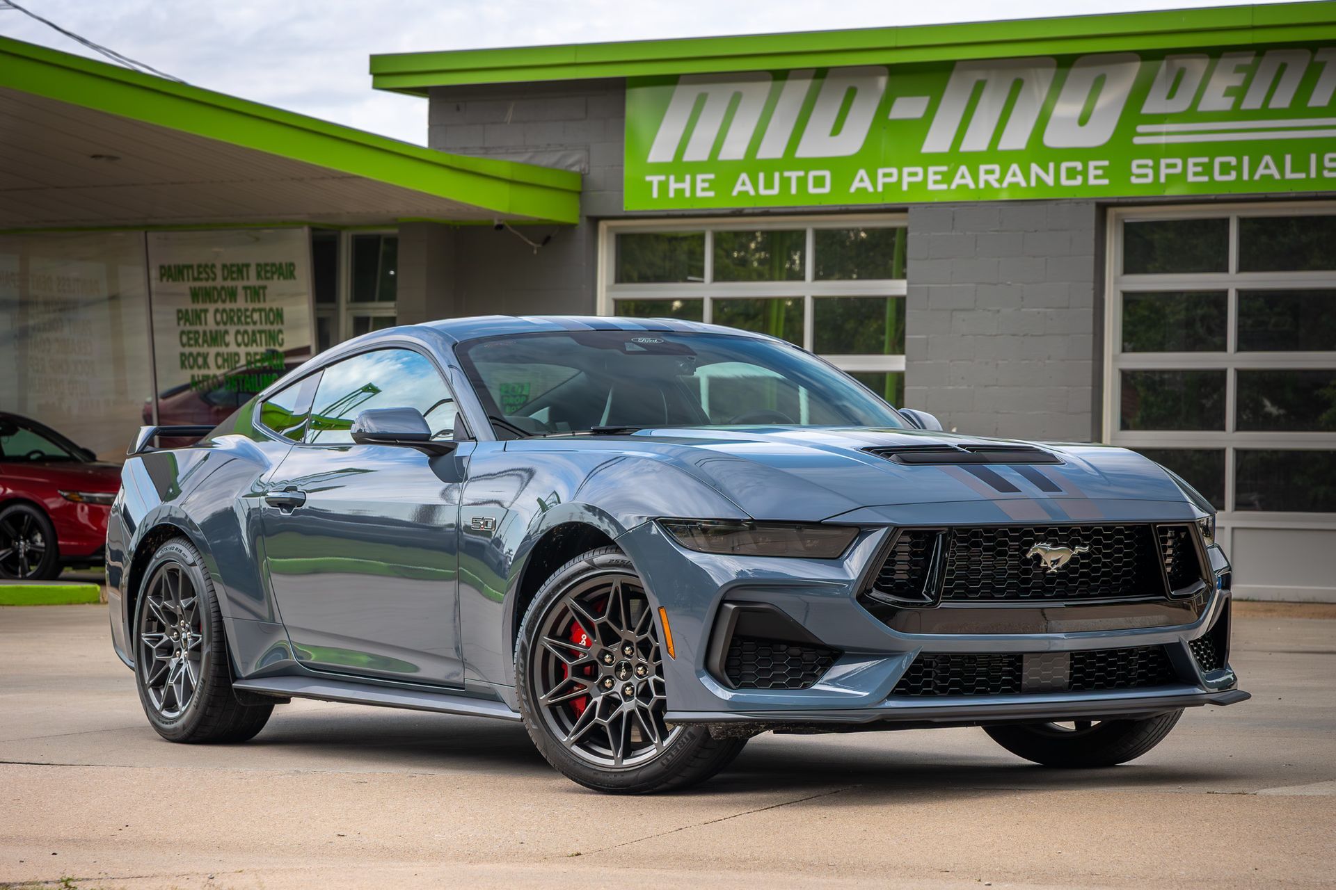 Gray Ford Mustang parked in front of an auto repair shop with a green sign.