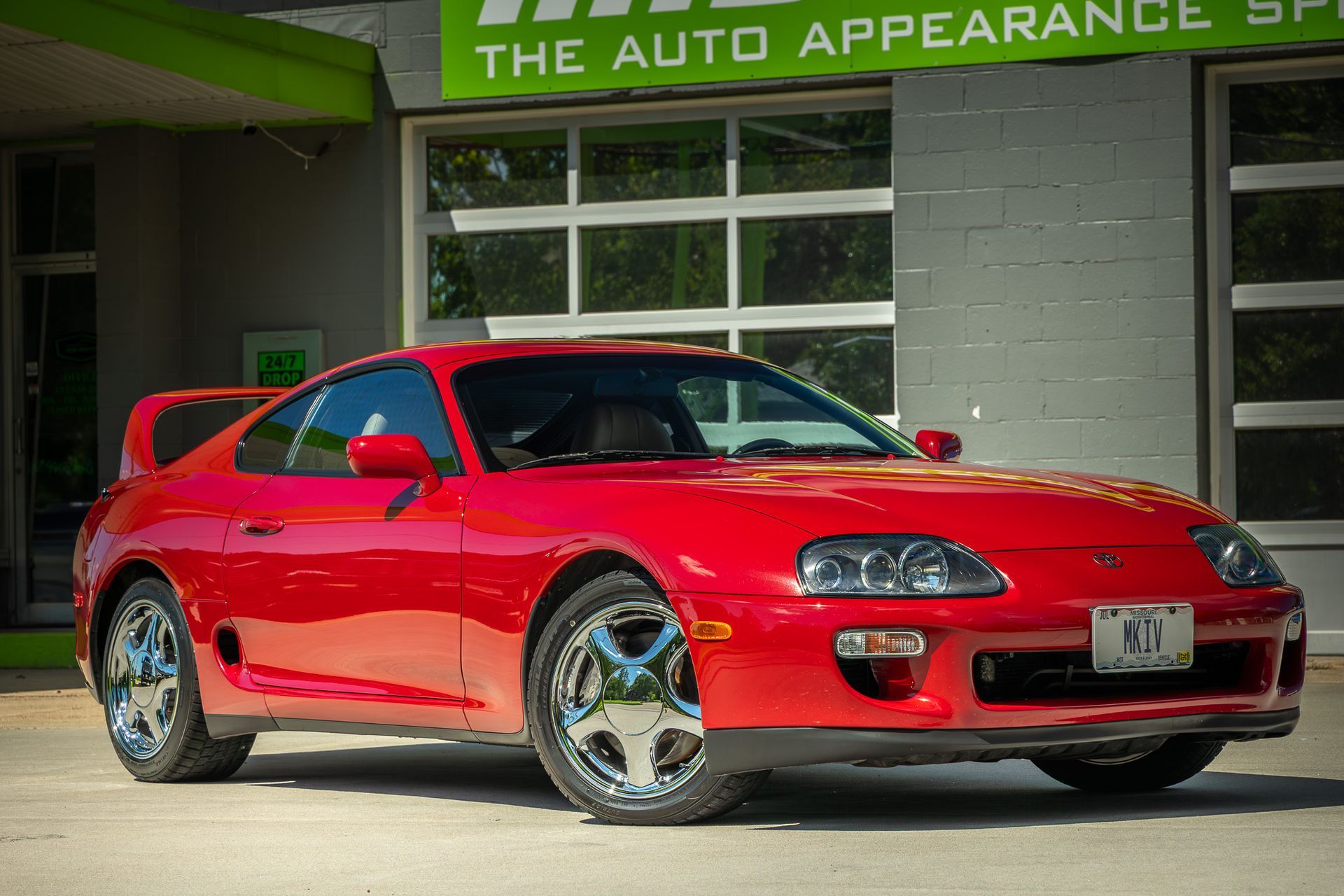 Red Toyota Supra parked in front of an auto appearance shop.
