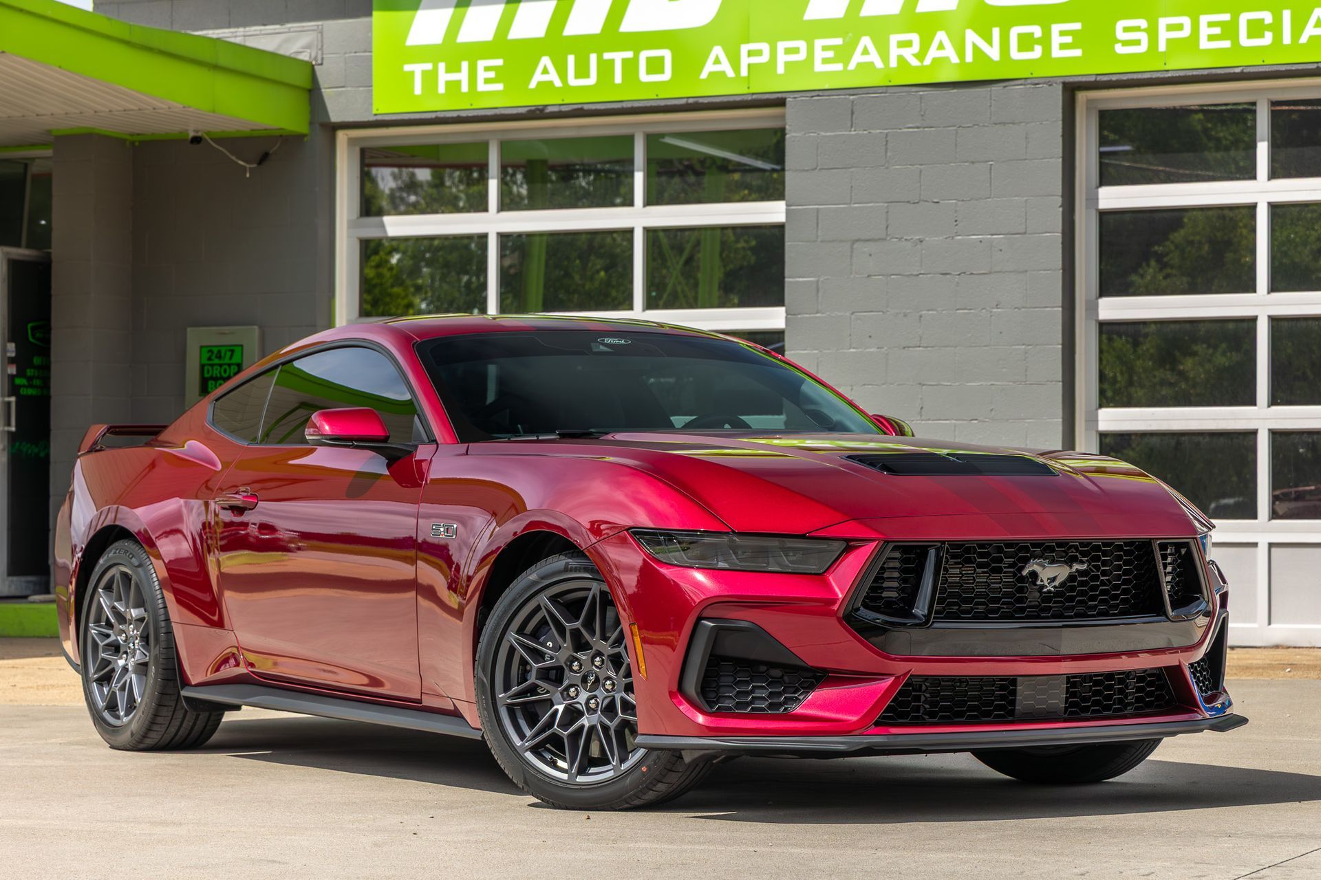 Red Ford Mustang sports car parked in front of a shop.
