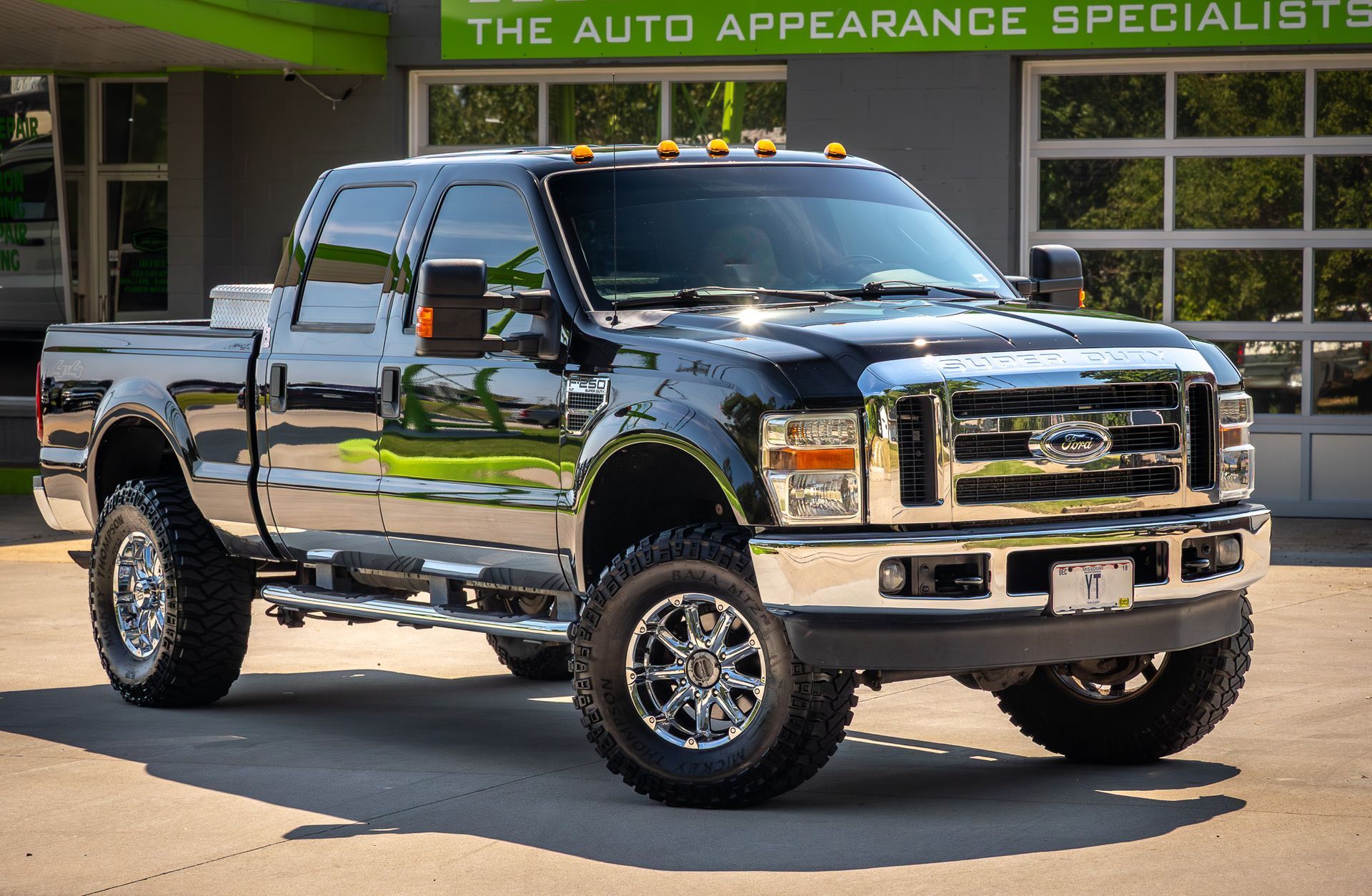 Black Ford F-Series pickup truck with chrome accents, parked in front of a building with a garage door.