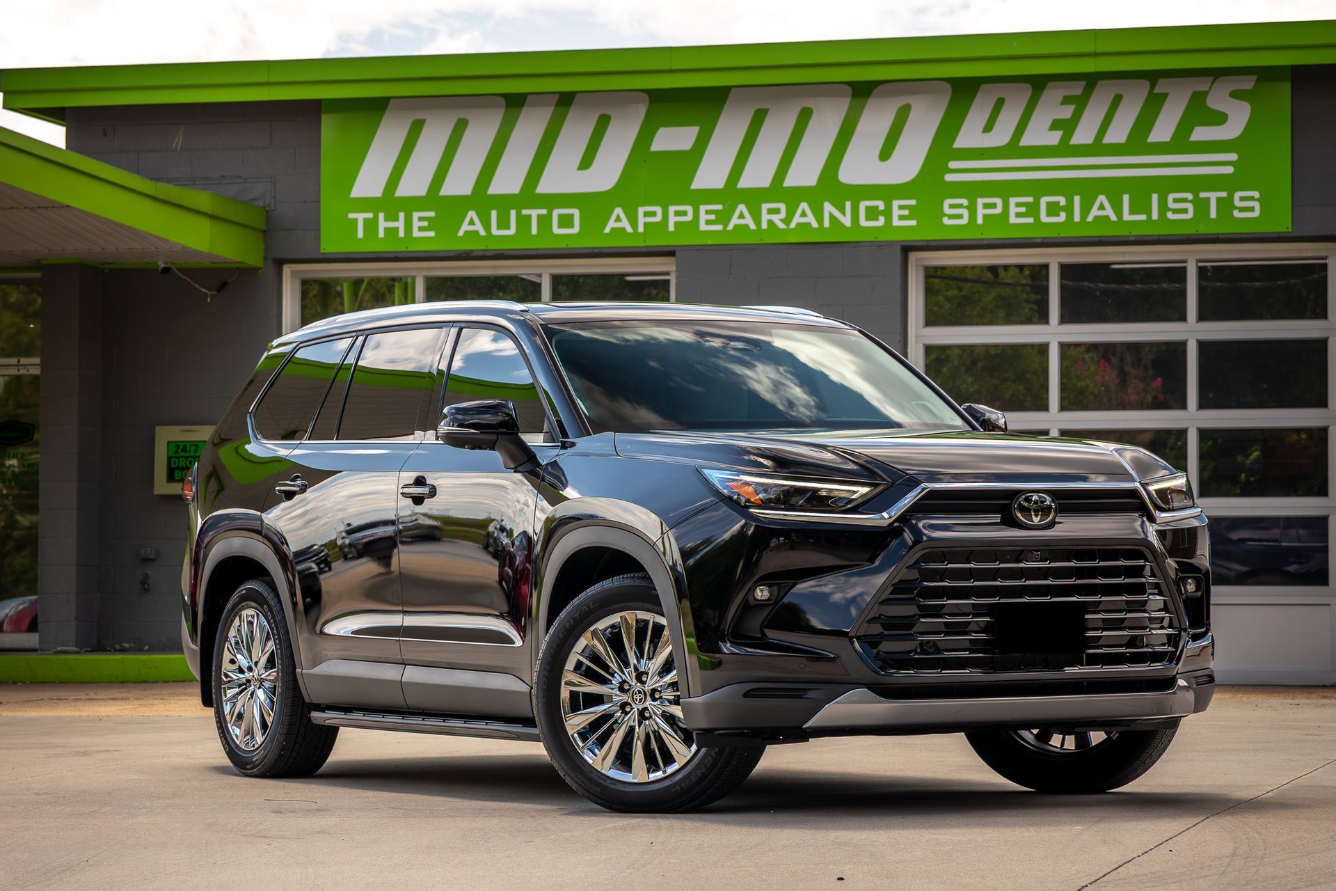 Black SUV parked in front of a green and gray auto body shop sign.