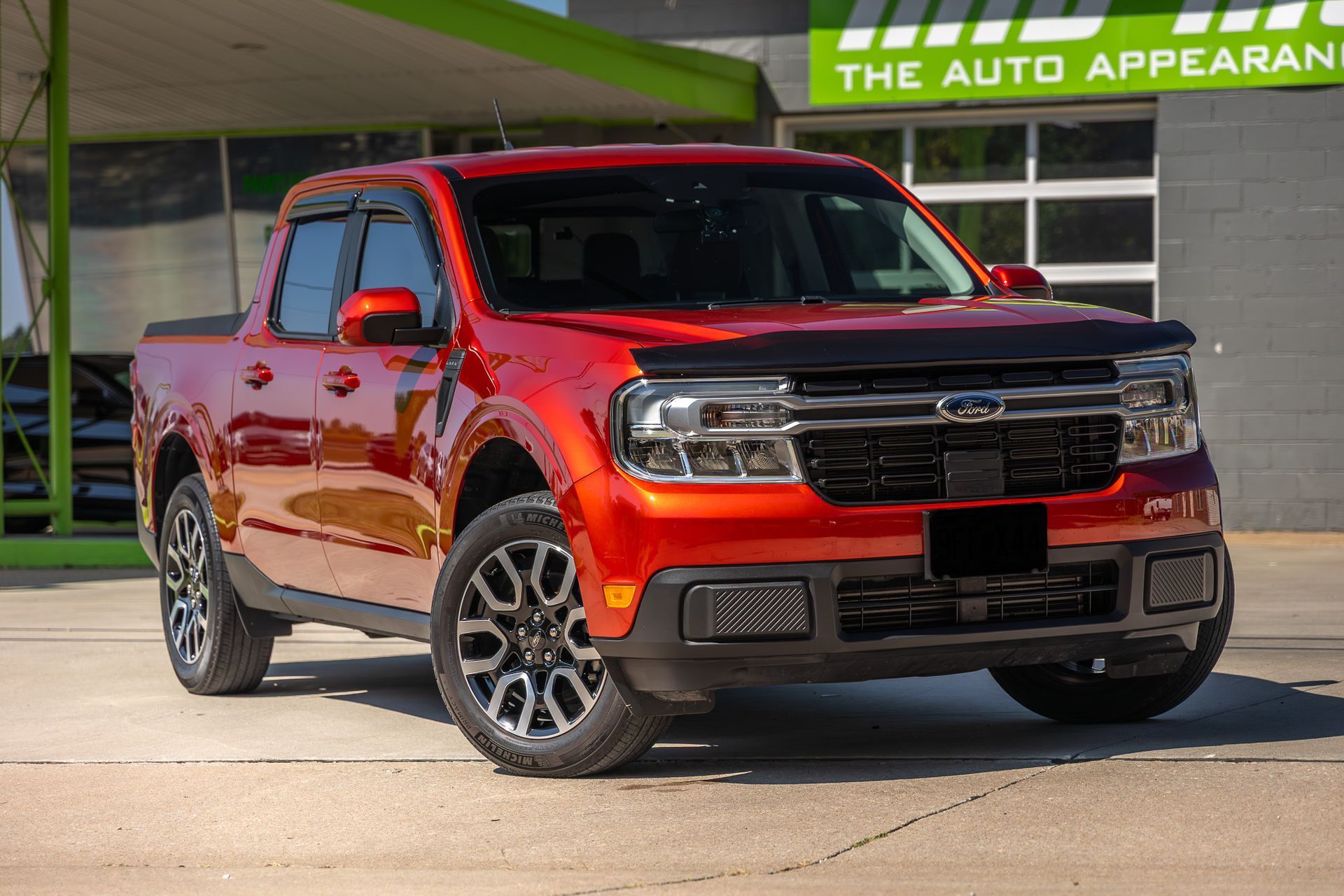 Red Ford Maverick pickup truck parked in front of a building with a green awning.
