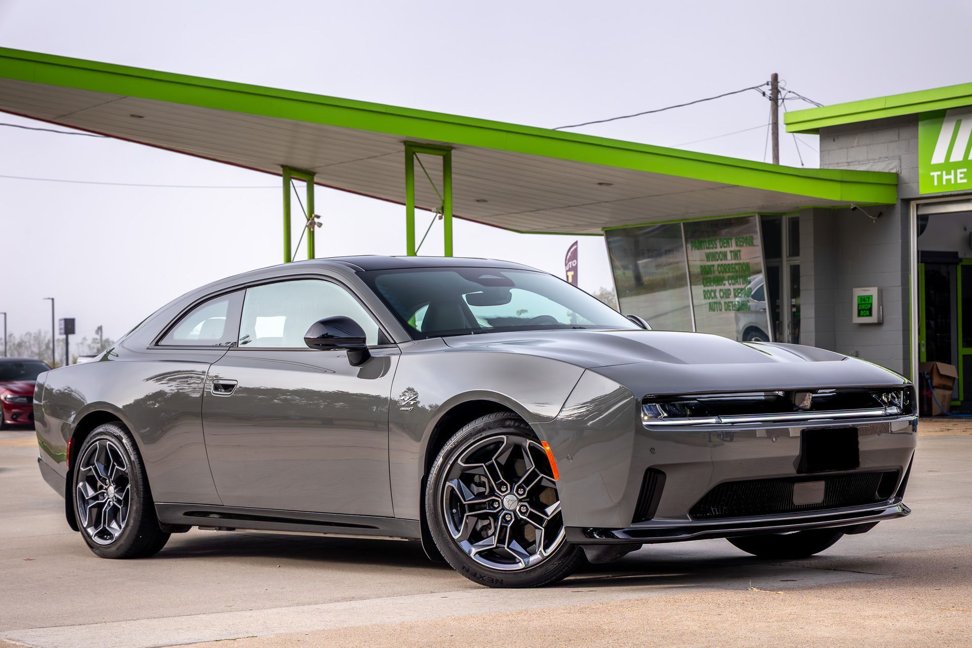 Gray two-door car parked outside a building with a green awning. The car has black wheels.