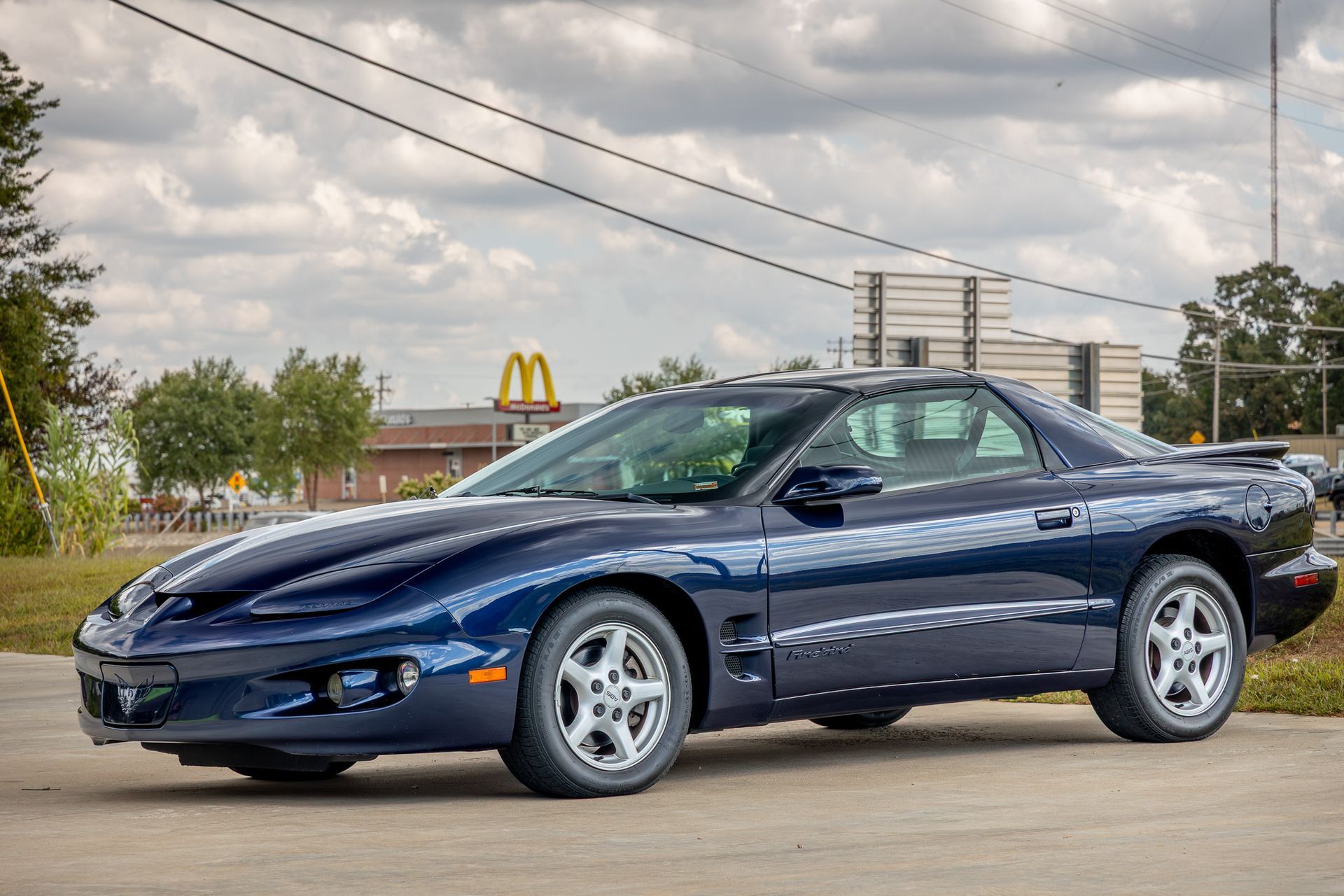 Blue Pontiac Firebird parked outdoors, partially obscuring a McDonald's restaurant.
