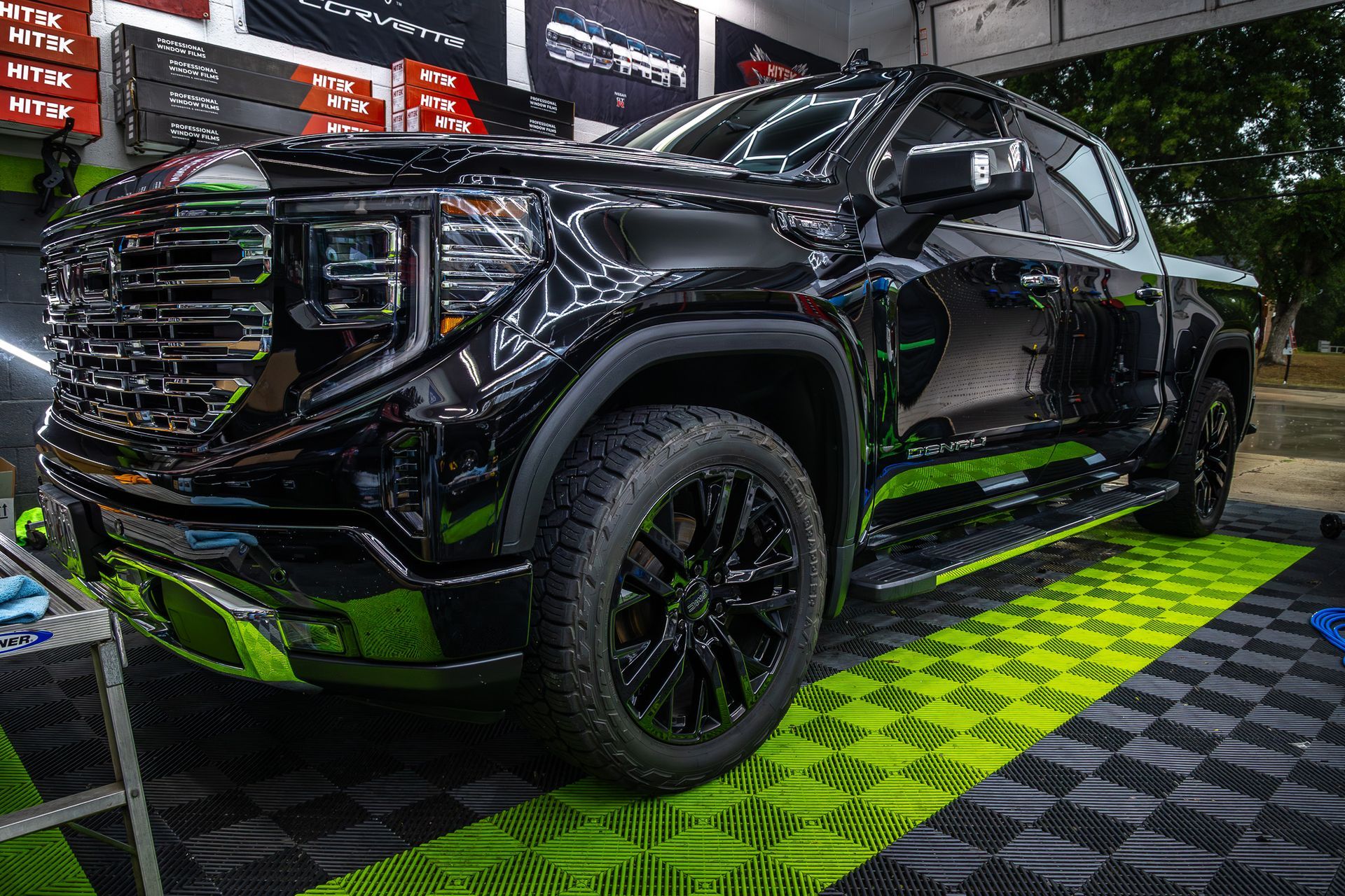 Black GMC Sierra pickup truck with black wheels on a checkered green floor, in a shop setting.