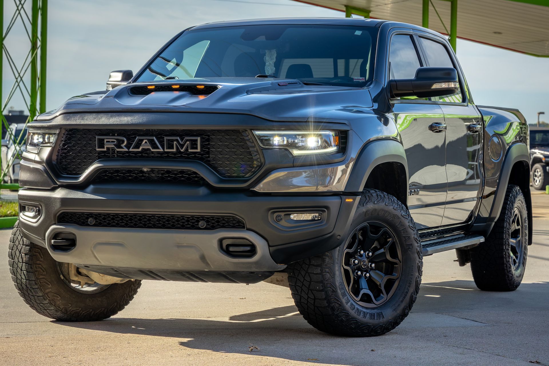 Black Ram TRX truck parked in front of a building with bright, focused headlights and off-road tires.