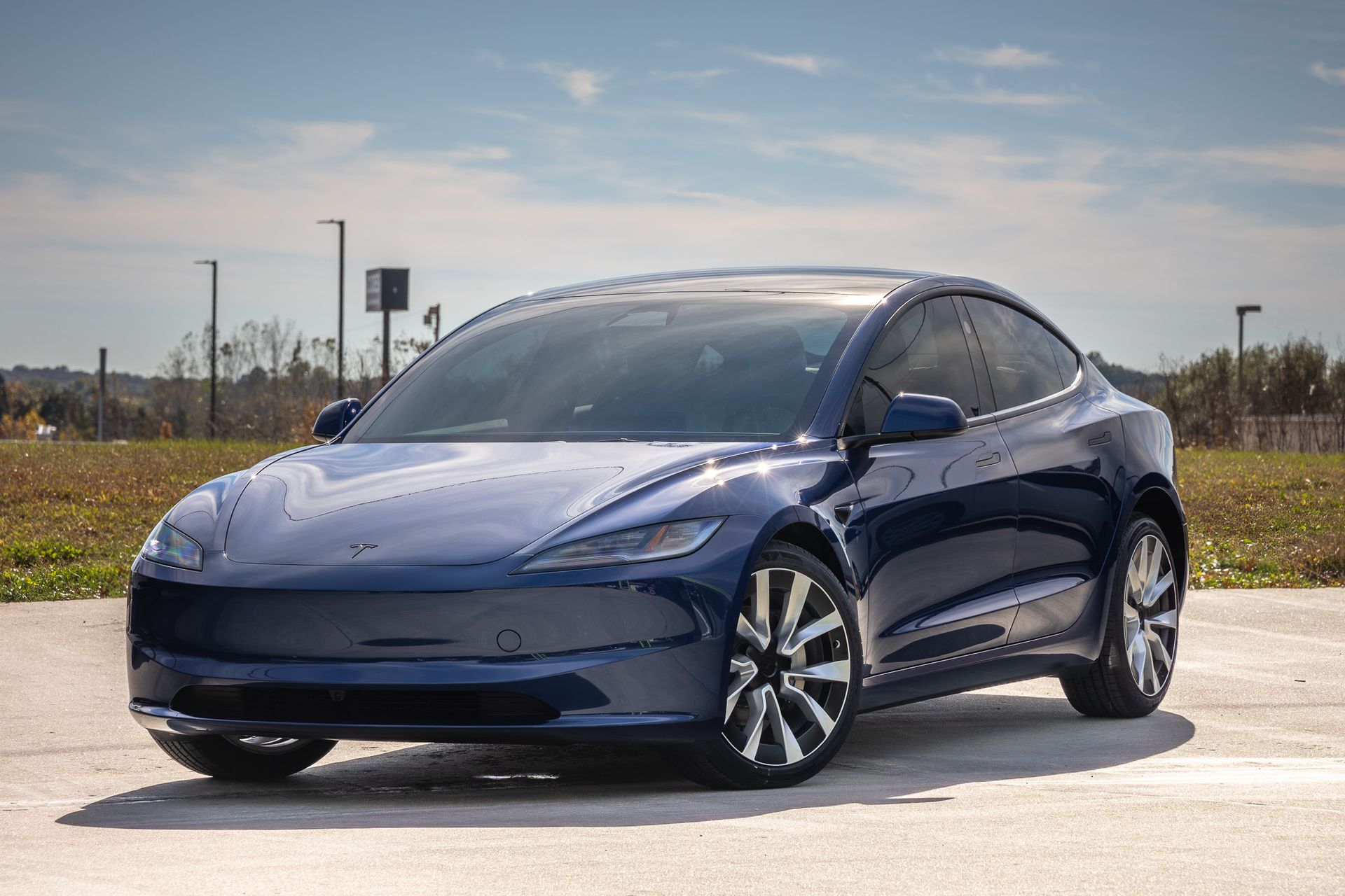Blue Tesla sedan parked on a concrete surface with blue sky in background.