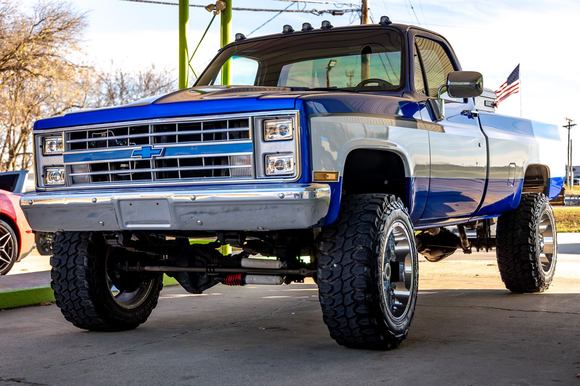 Blue and silver lifted Chevrolet truck with large tires, parked outdoors.