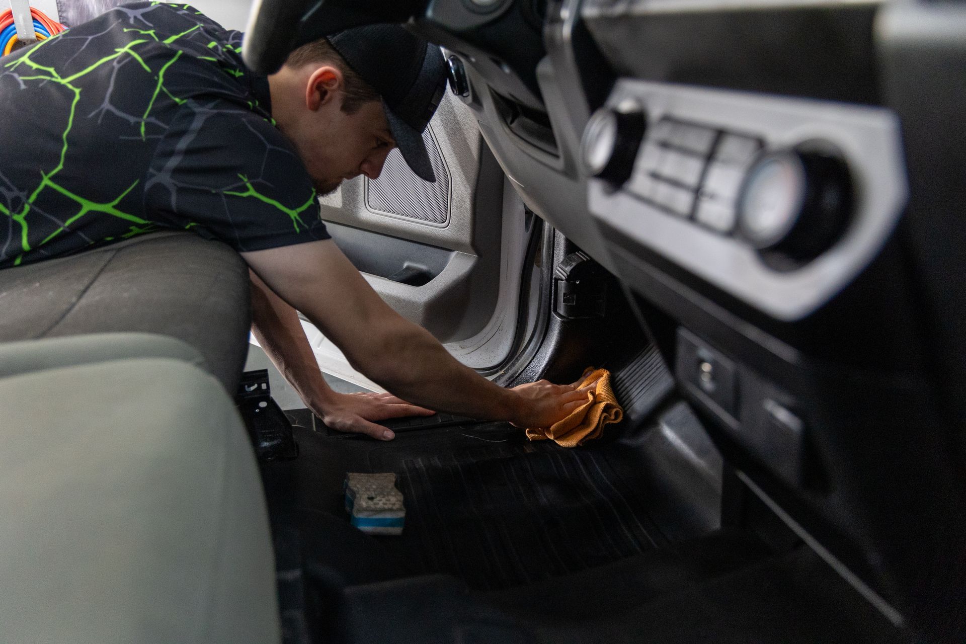 Man cleaning the interior of a vehicle with an orange cloth.