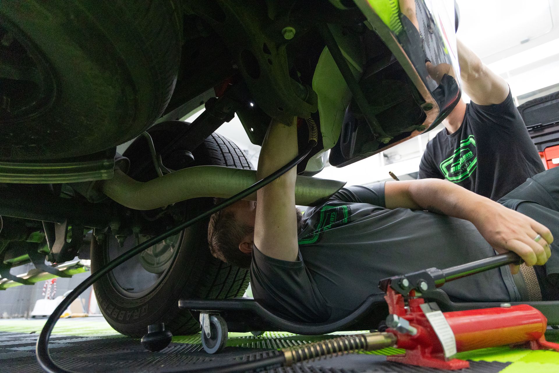 Two dent techs using a port-o-power to push out the bulk of a dent in a truck bedside.
