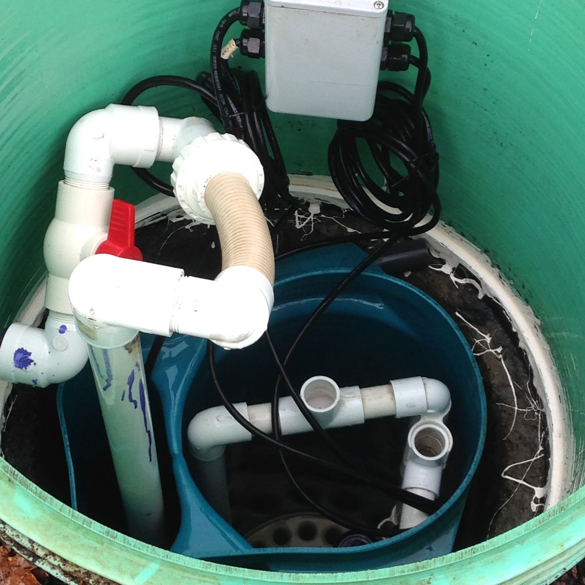 Green septic tank interior with white PVC pipes, red valve, pump, and electrical box.