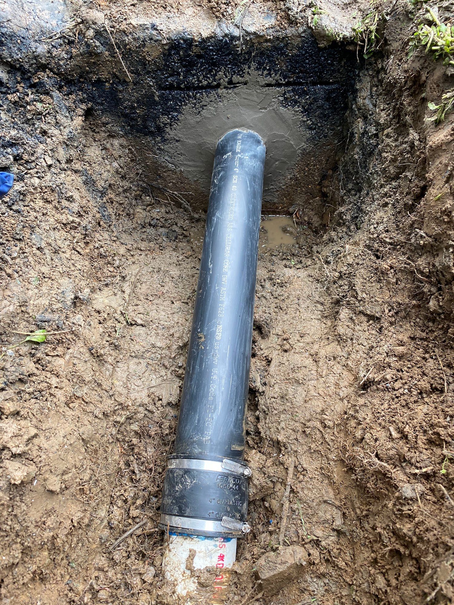 Black pipe in a dirt pit, with a concrete base.