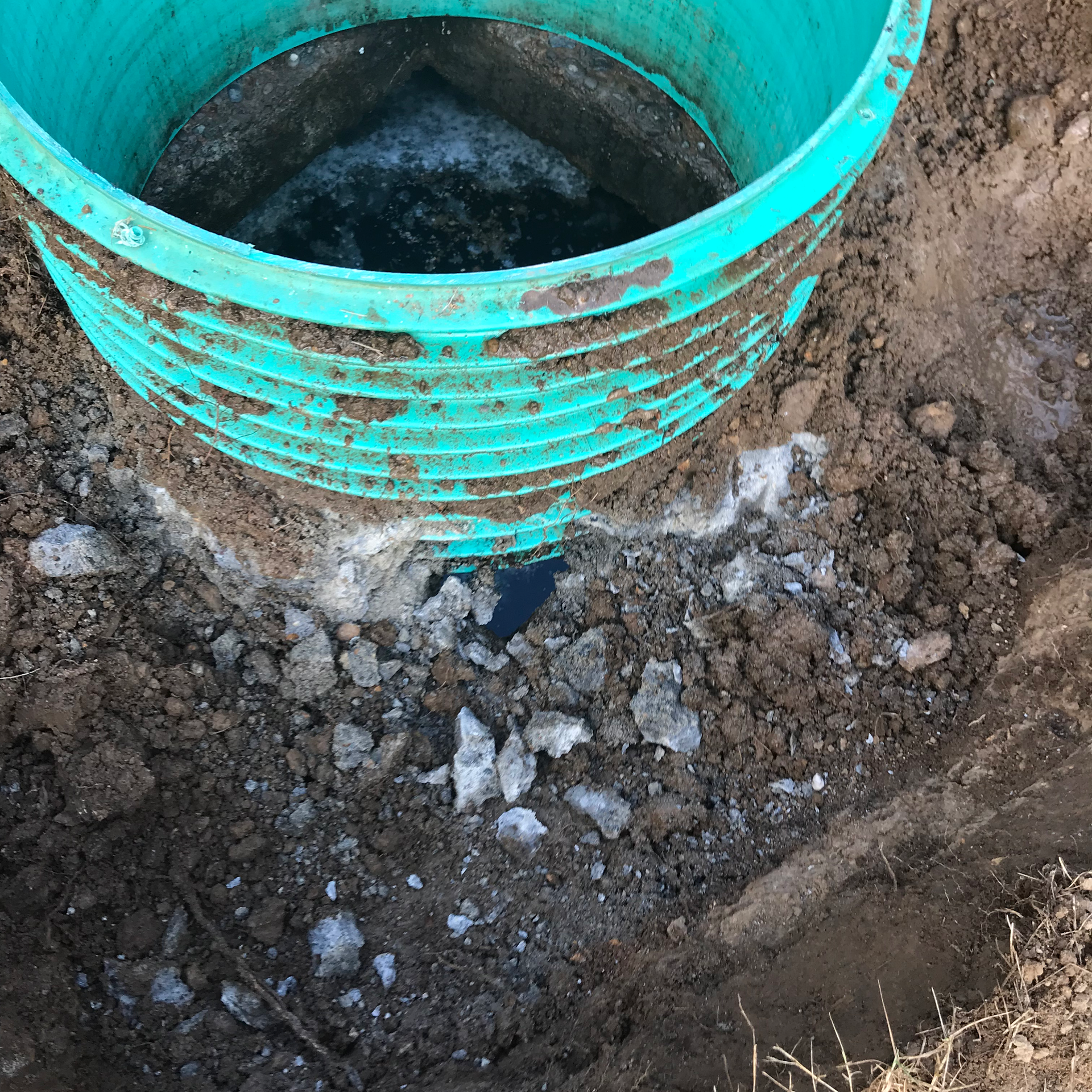 Green plastic cylinder in a hole dug in the dirt, with rocks and water visible.