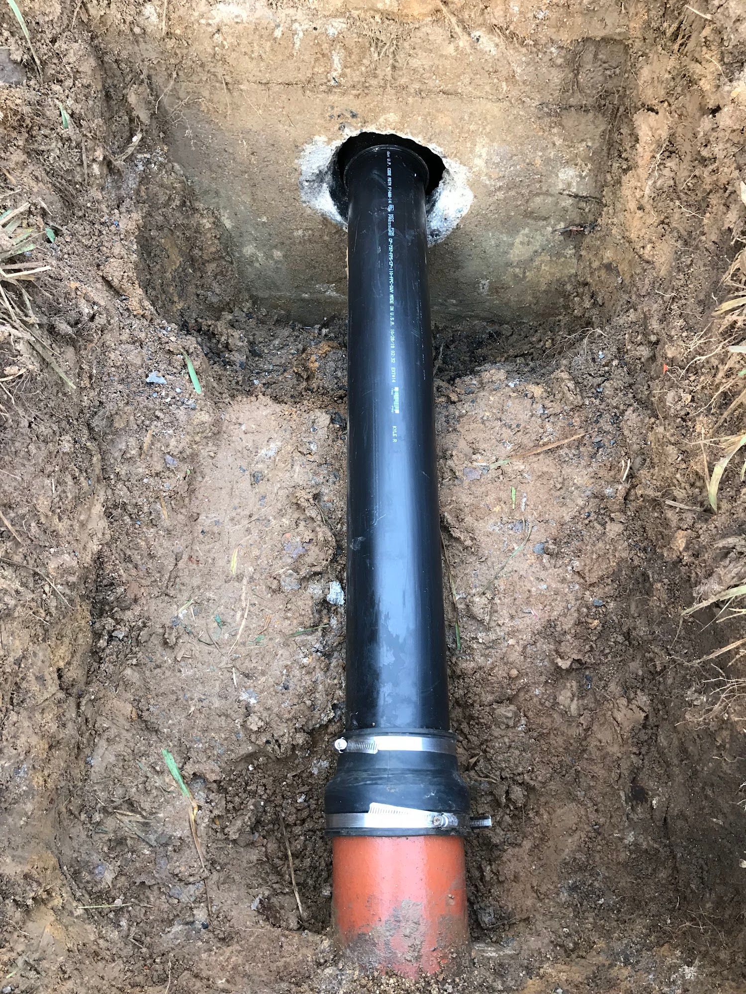 Black pipe extending from ground, surrounded by soil. Orange pipe connected at the bottom.
