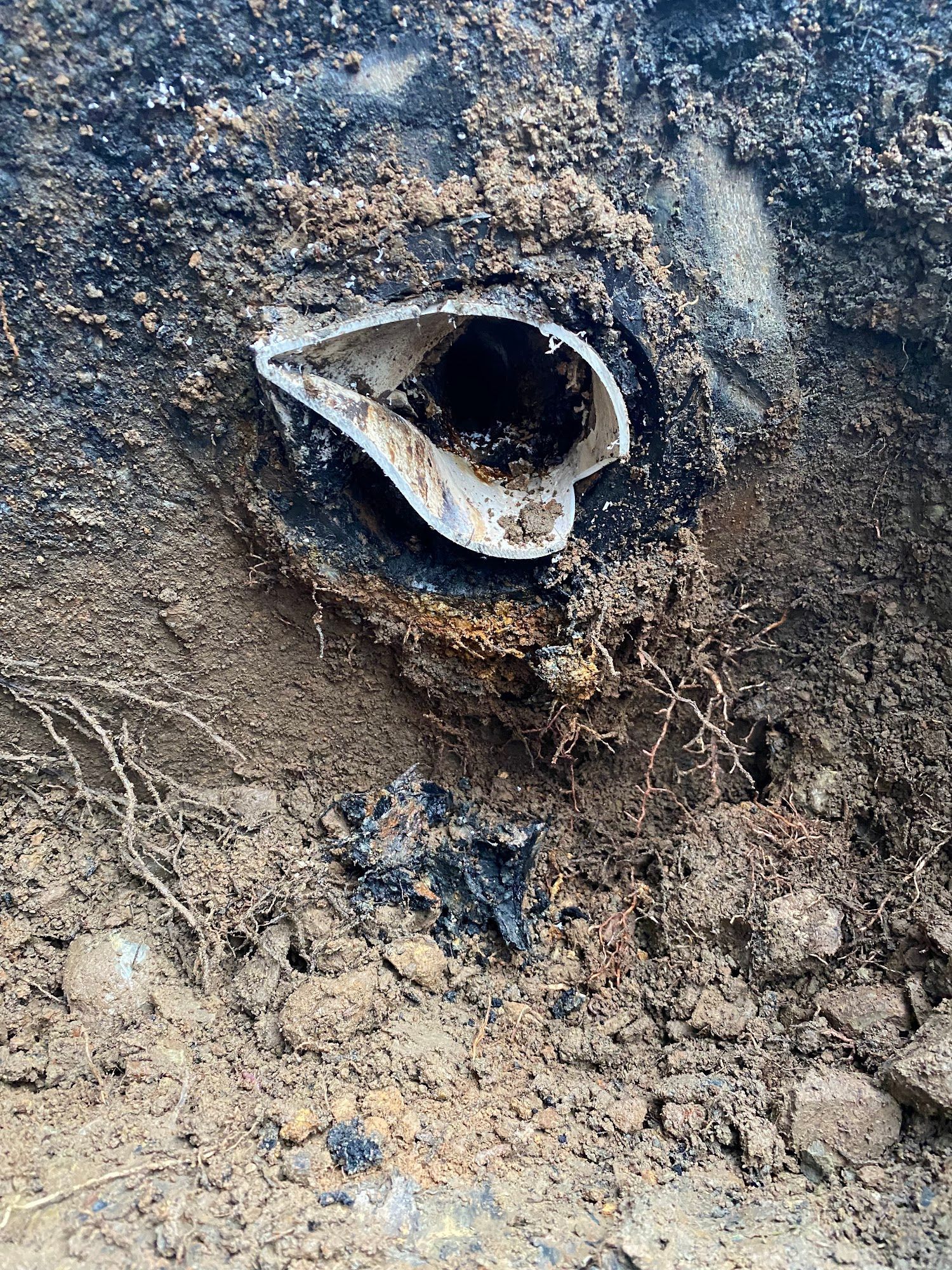 Broken white plastic pipe in dark soil, revealing a black pipe beneath.