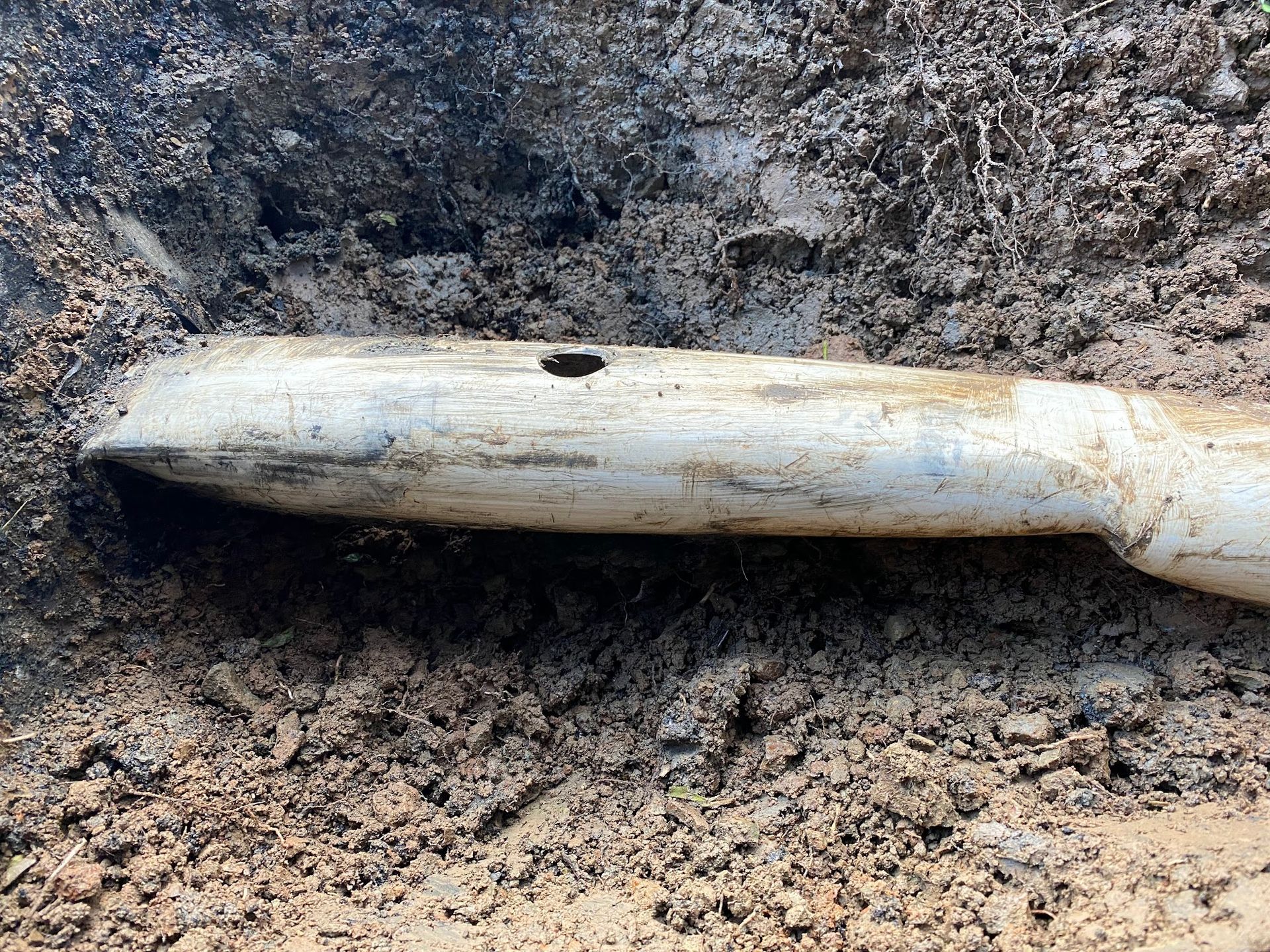 White plastic pipe with a hole in it, exposed in a dirt trench.