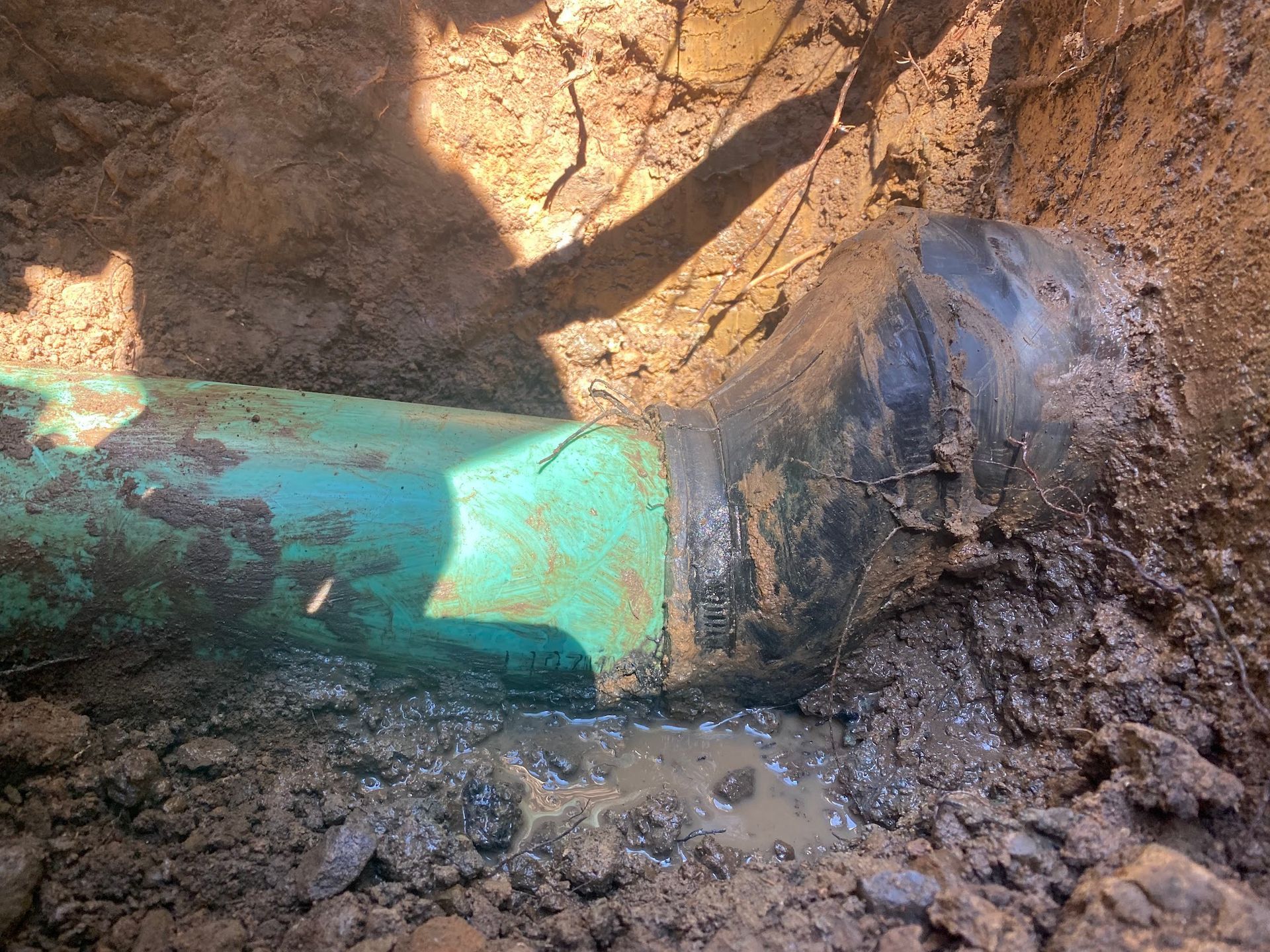 Green pipe with a leak in a dirt trench.