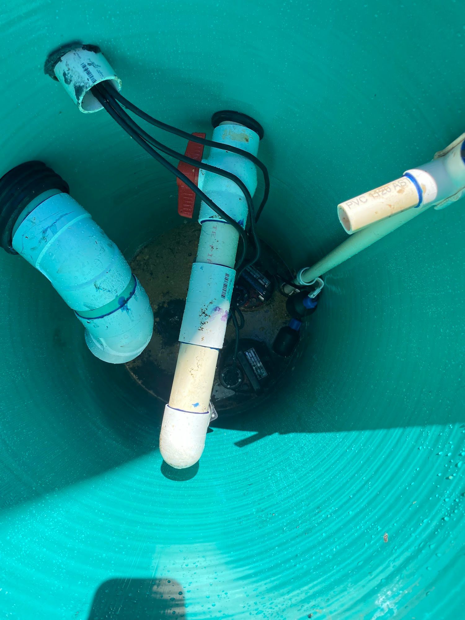 View inside a green water tank with plumbing, electrical wires, and a pump.