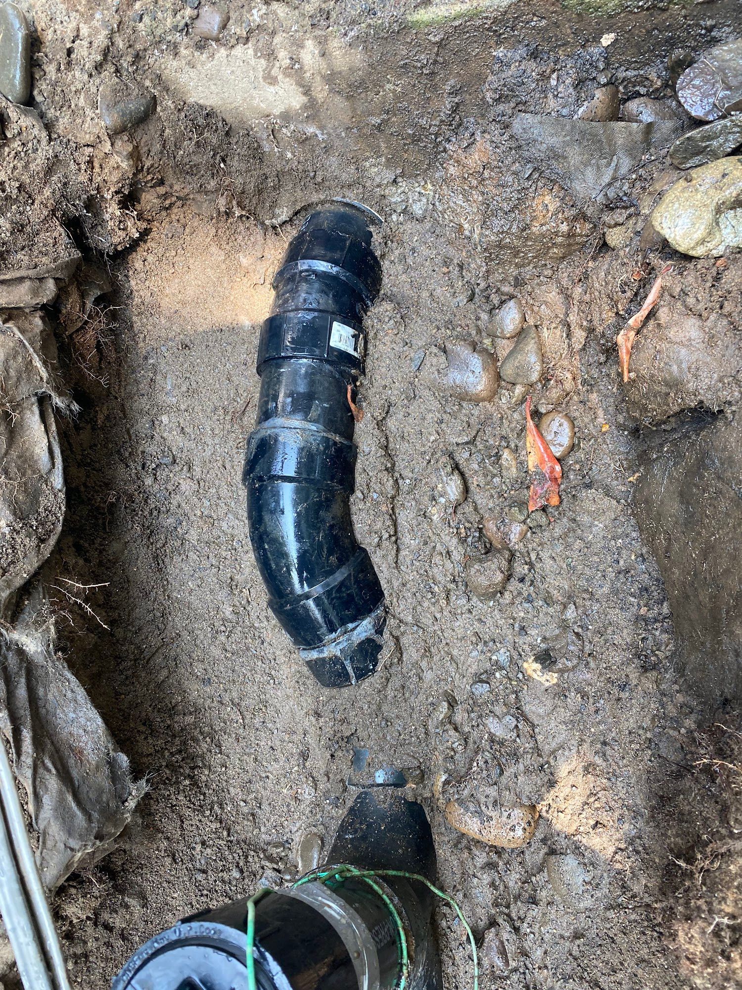 Black plumbing pipes partially buried in dirt.