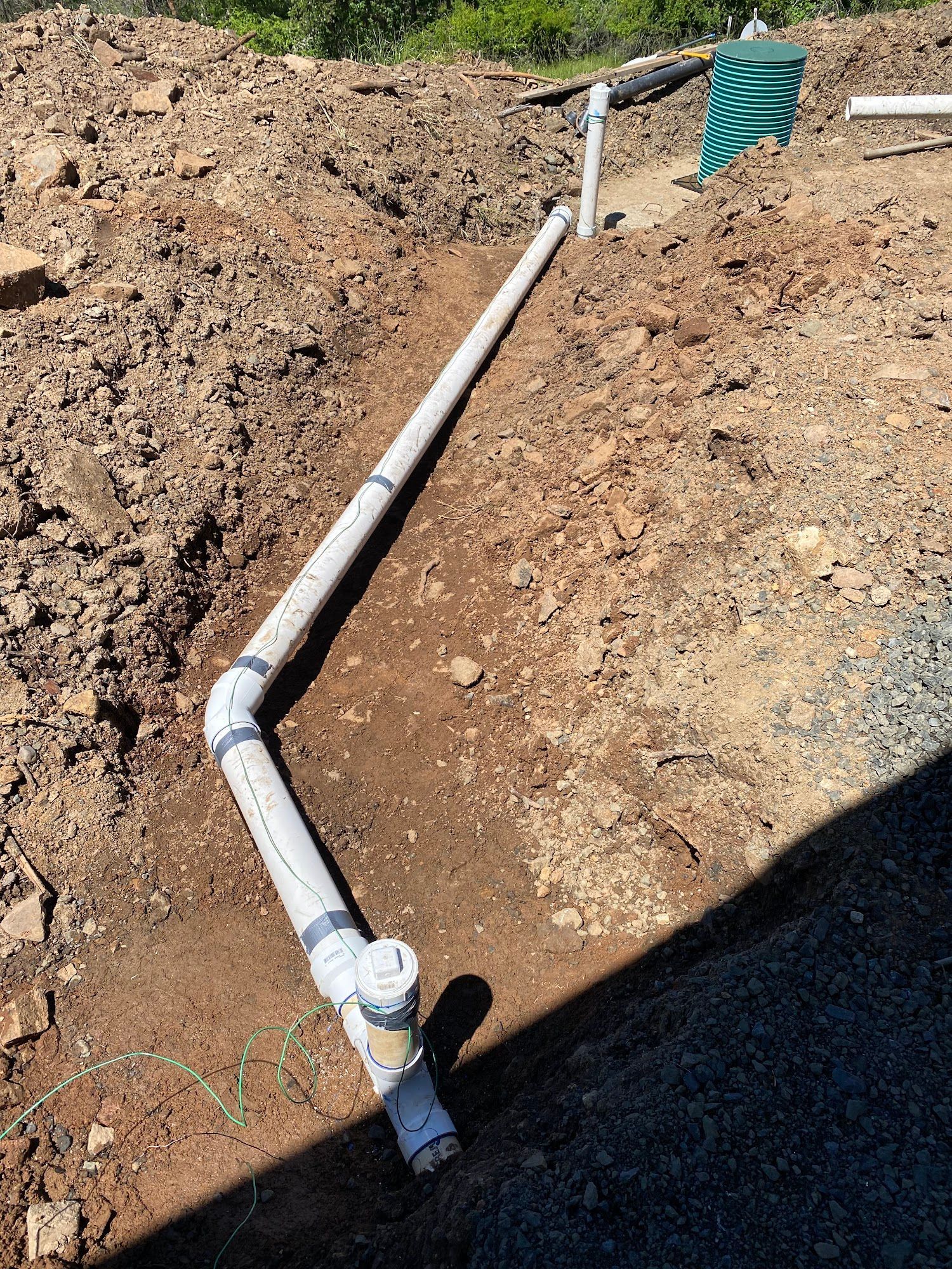 PVC pipes in a trench, likely for drainage or utility. Dirt surrounds the pipes.