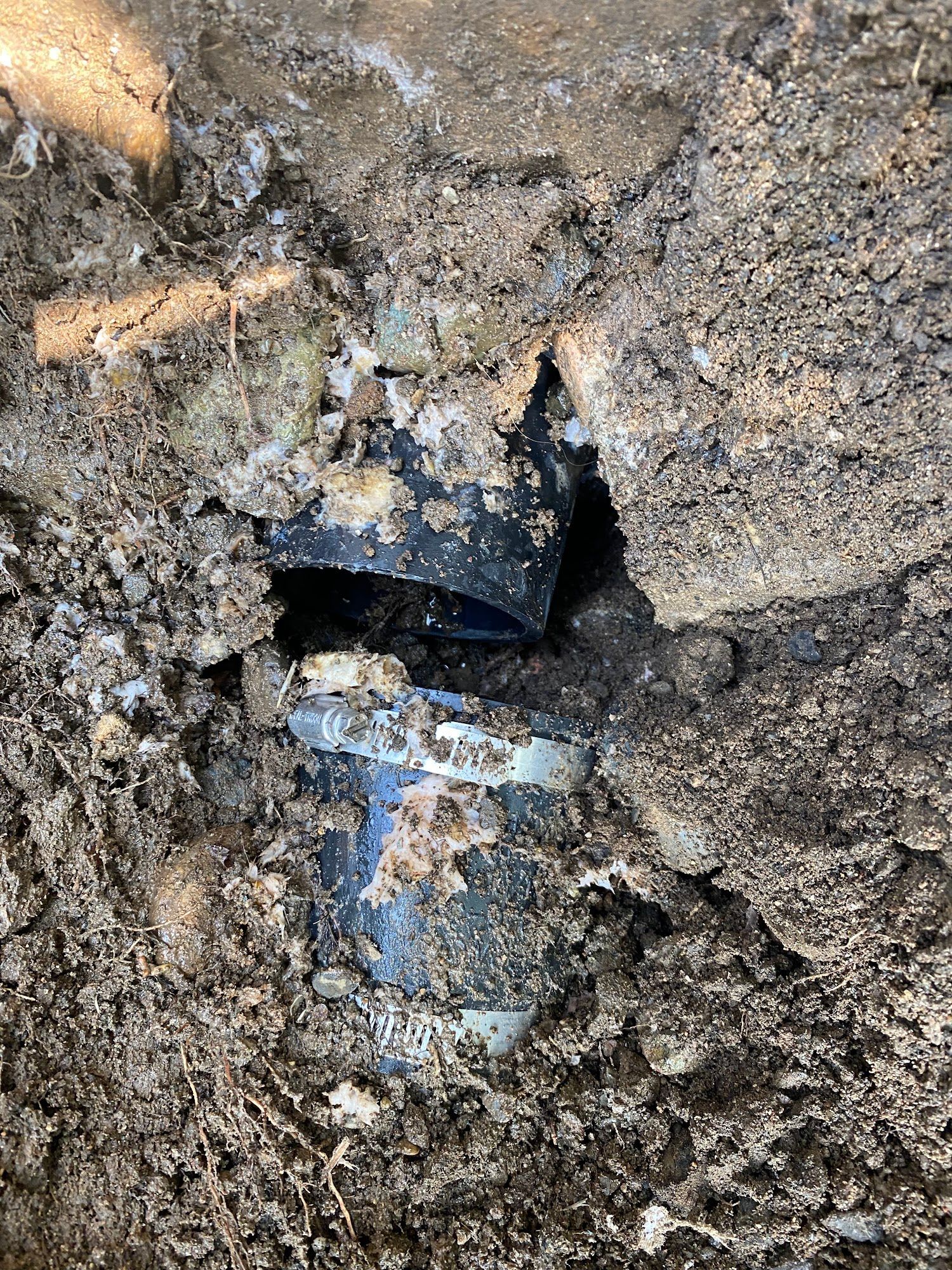 Broken black PVC pipe in muddy soil.