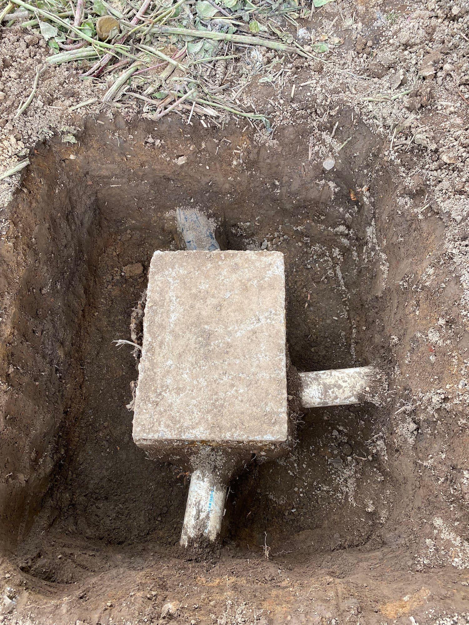 Concrete box with white pipes in a square dirt excavation.