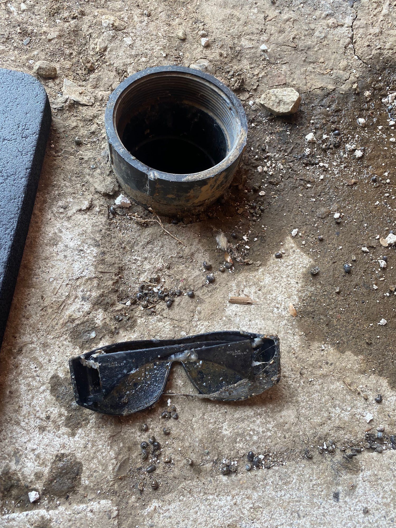 Black sunglasses and pipe opening on a concrete surface.