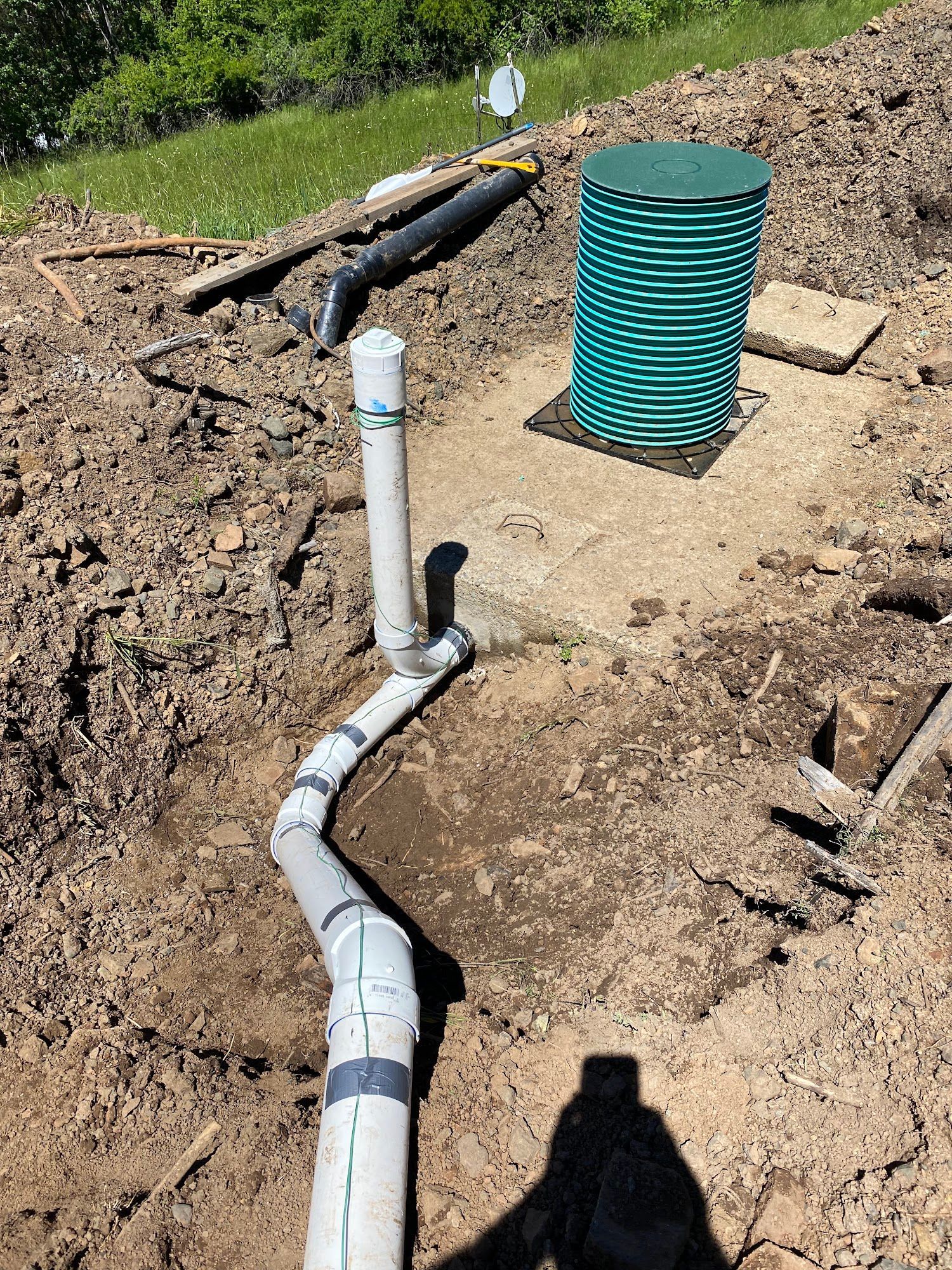 Pipes and green tank in dirt, likely a septic system installation outdoors.