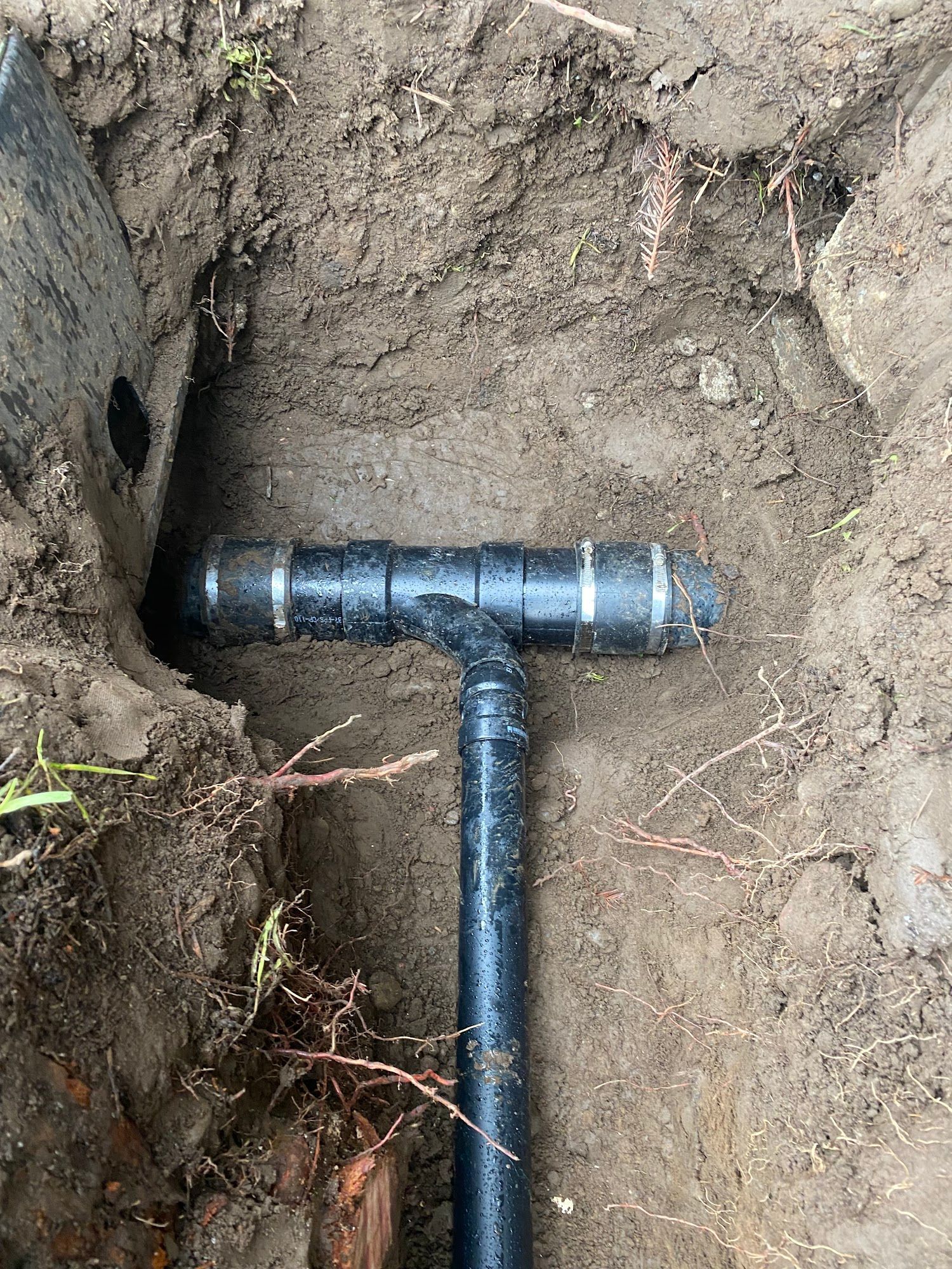 Black plumbing pipe with a T-joint, buried in dirt.