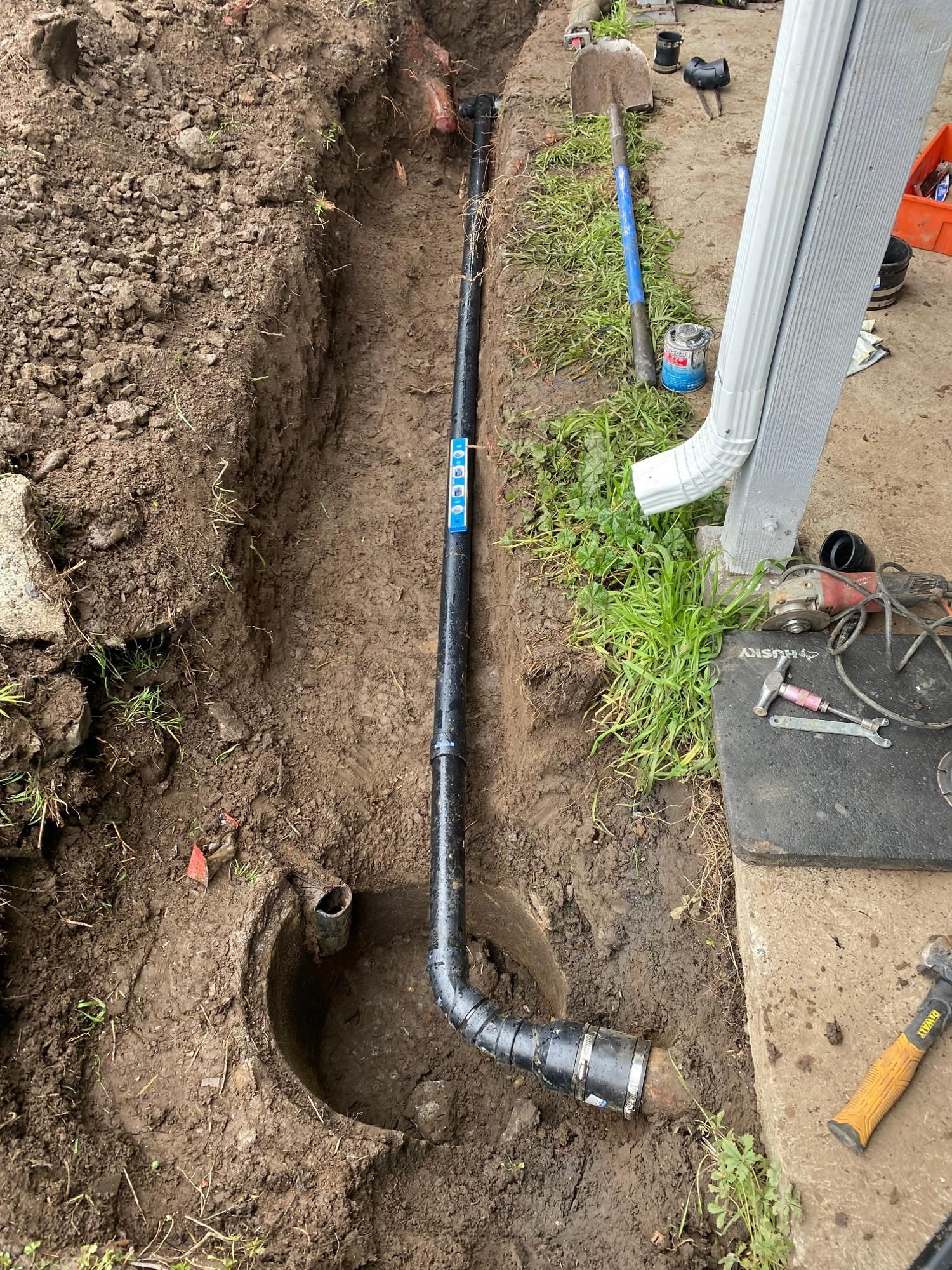 Black pipe installed in a trench next to a house with tools and dirt.