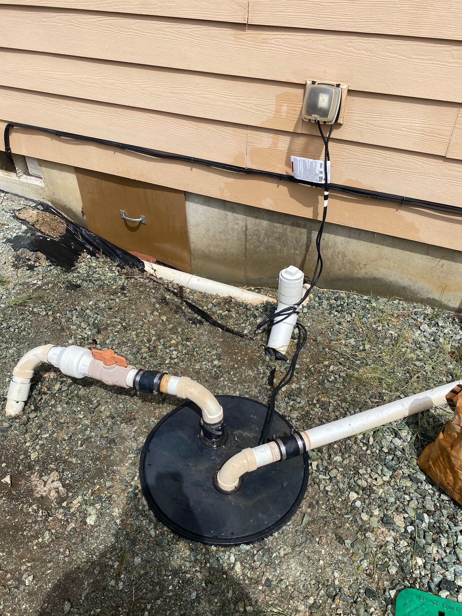 Black sump pump with connected pipes and electrical box on a building's exterior.
