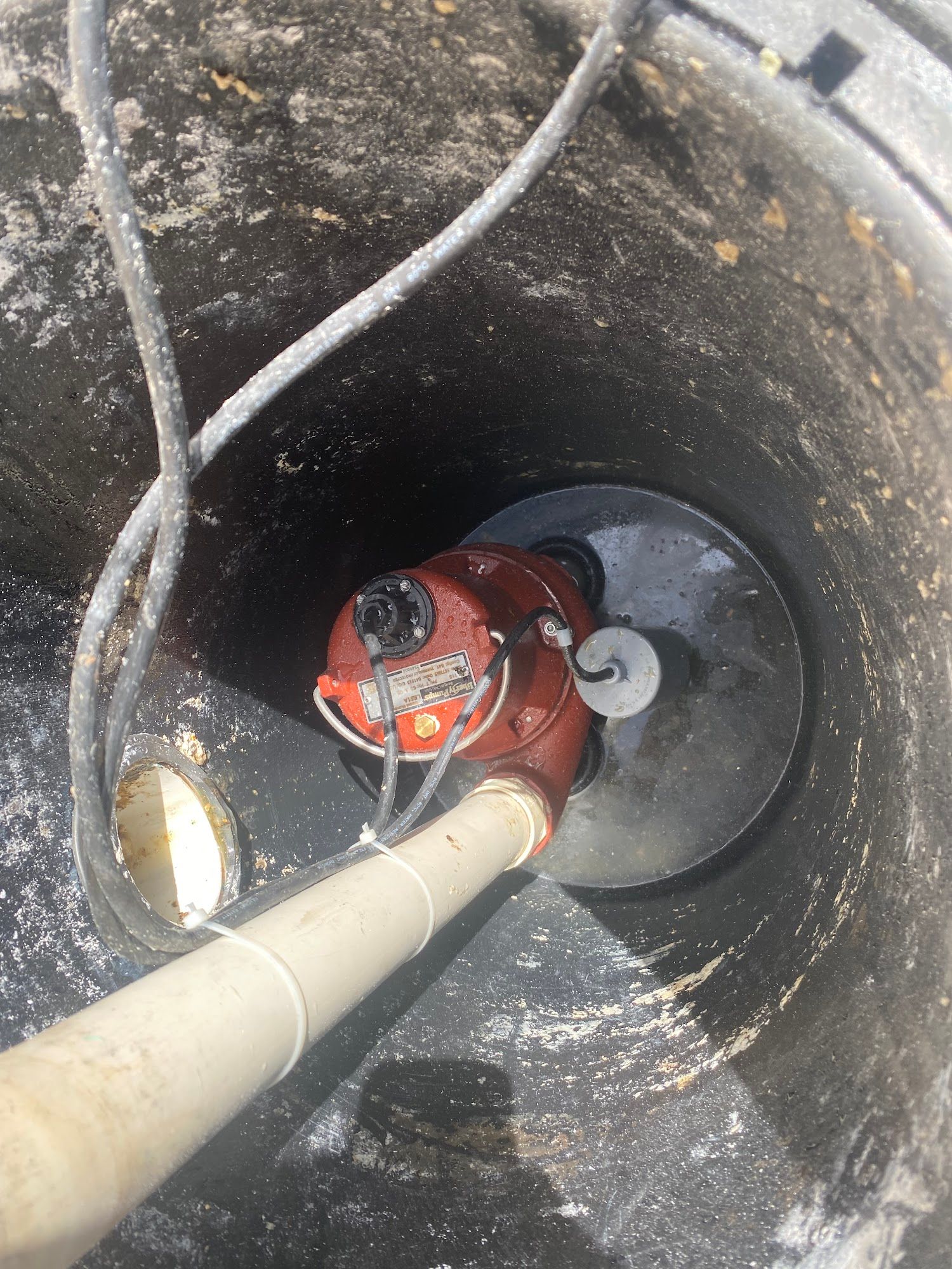 Inside a dark sump pit: A red pump with attached gray pipe and electrical wires.