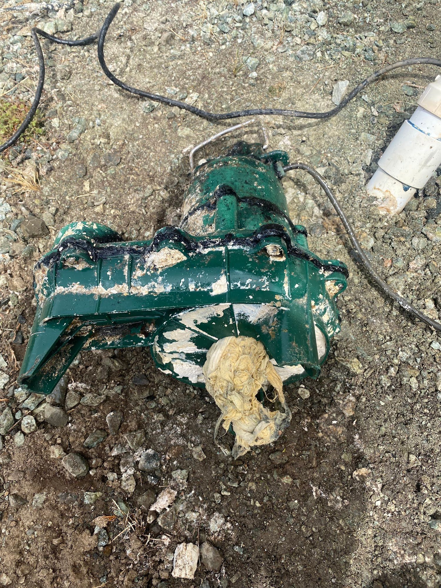 Green sump pump covered in mud lies on dirt.