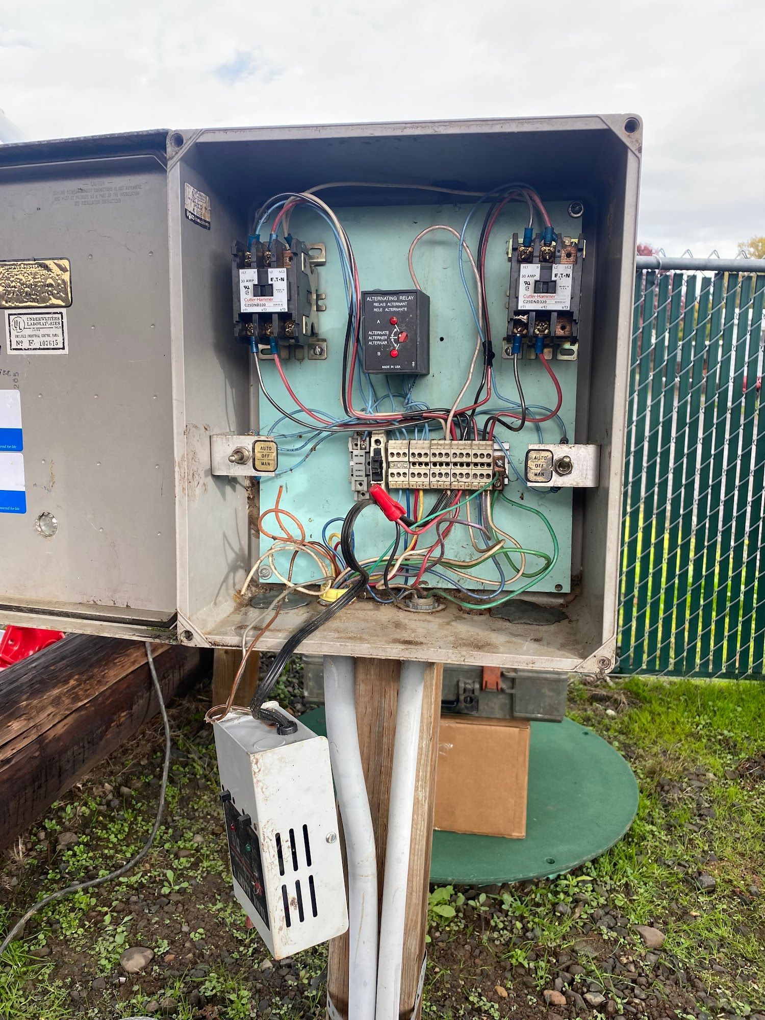 Open electrical panel with exposed wires and components mounted on a wooden post outdoors.