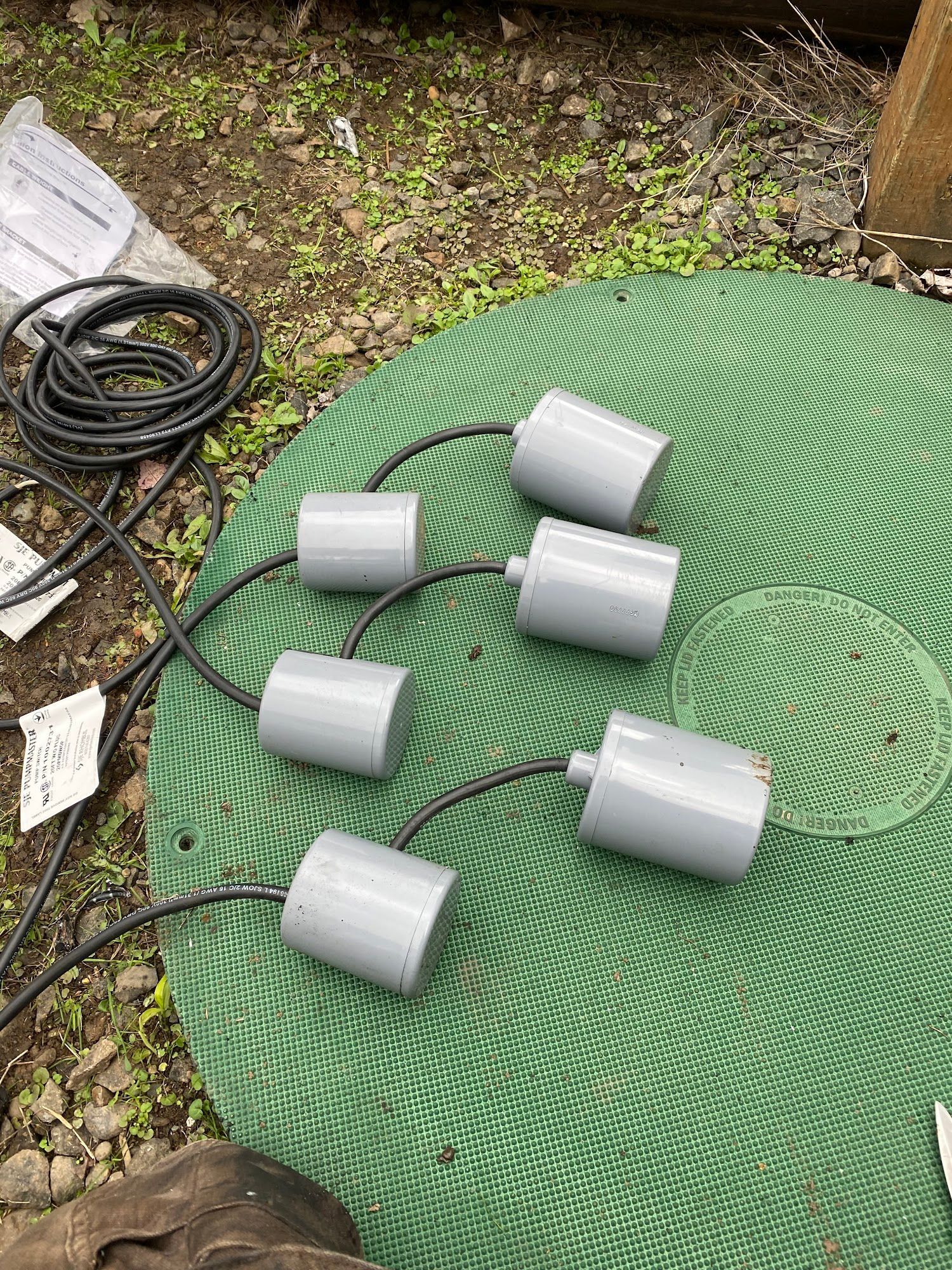 Six gray cylindrical objects with black cords on a green mesh surface. A black cable and paper are in the background.