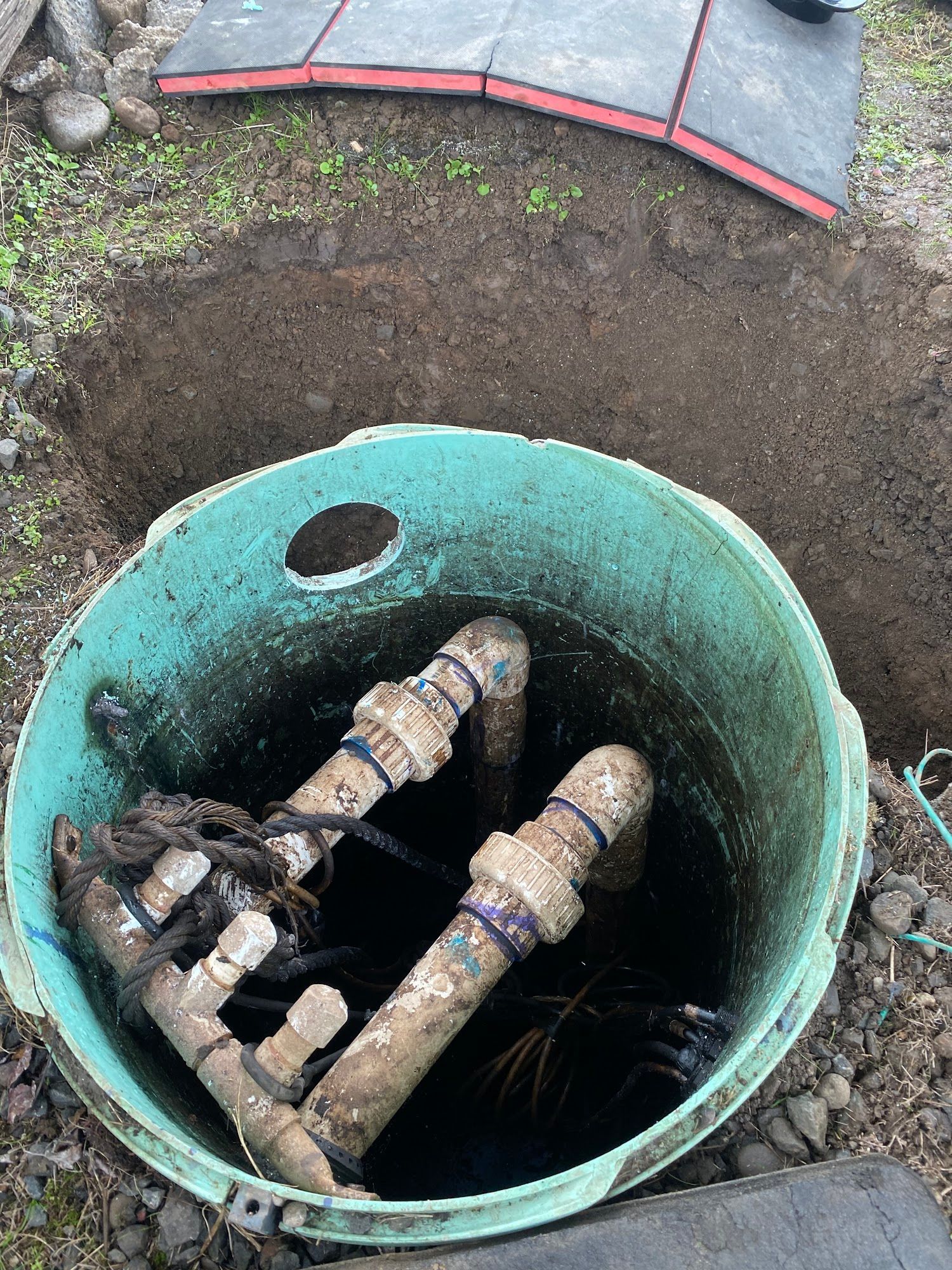 Open septic tank in an excavated hole, showing pipes and standing water.