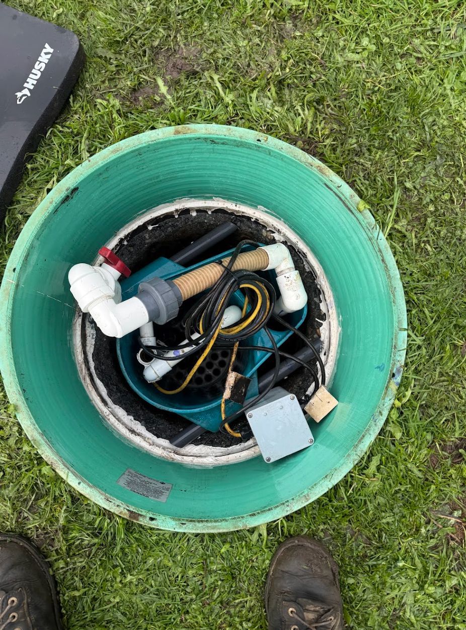 Open green bucket on grass holding coiled cables, pipes, and a small electrical box