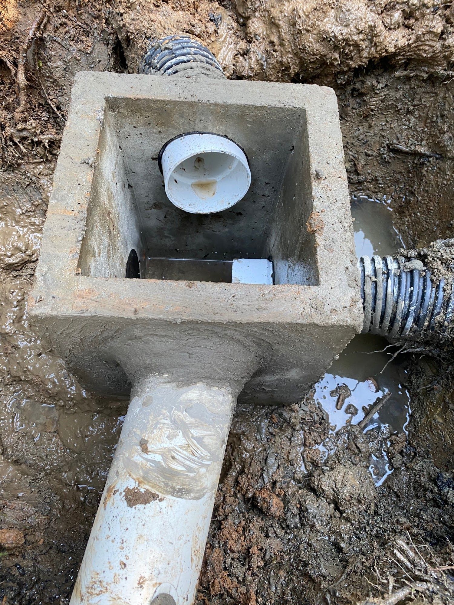 Concrete drain box with pipes in muddy ground.