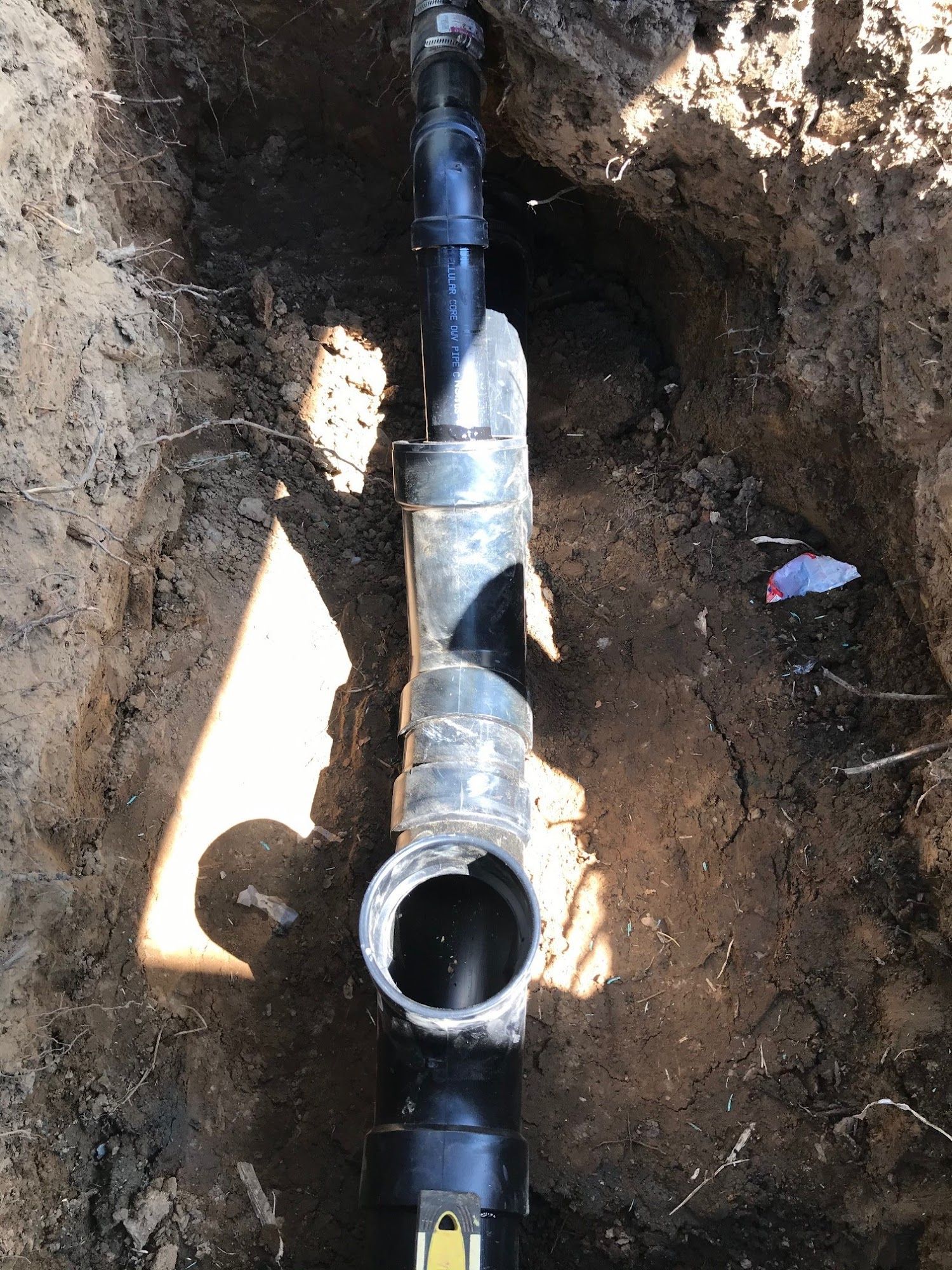 Black and silver plumbing pipes in a trench.