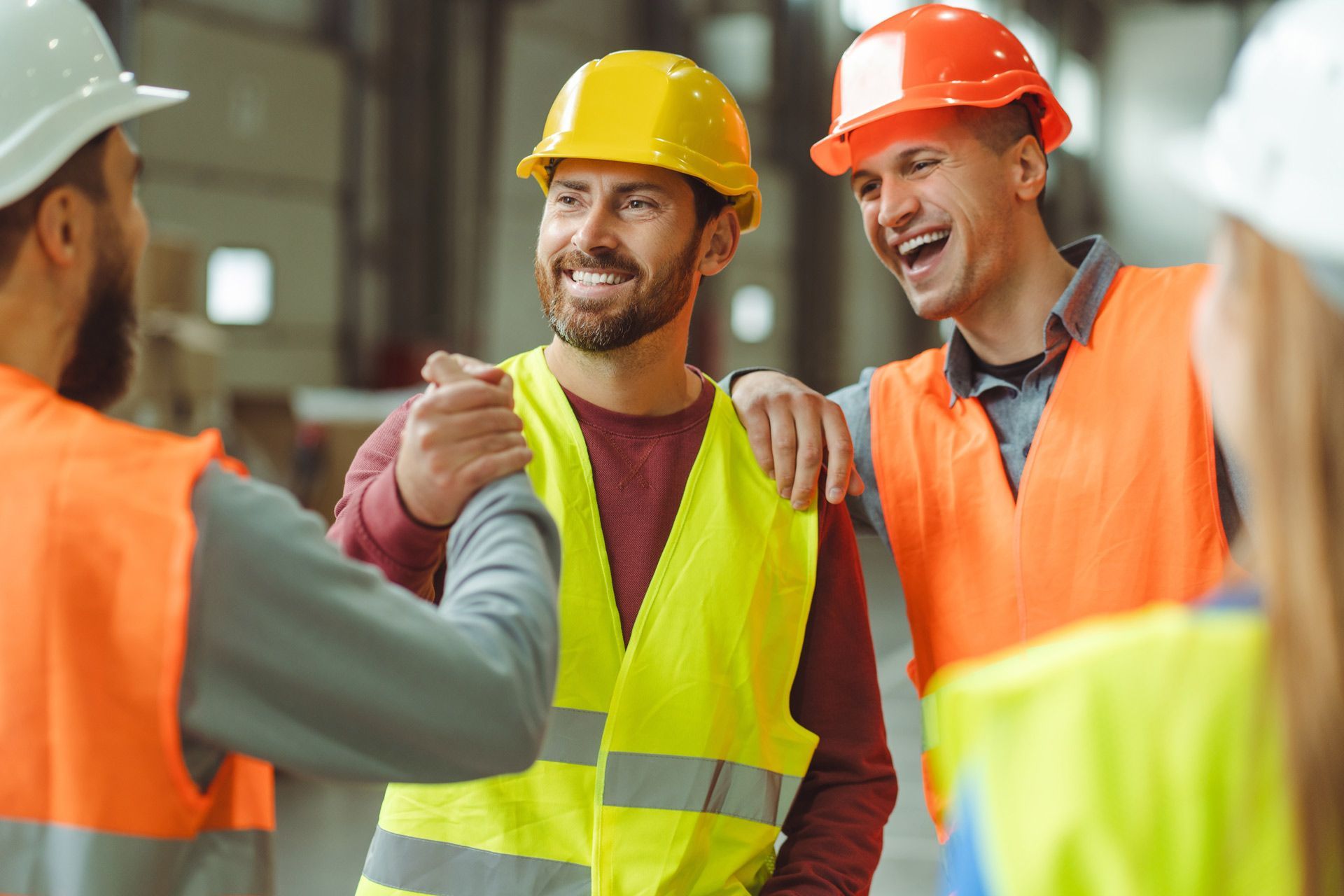 Construction workers in safety gear, laughing and shaking hands.