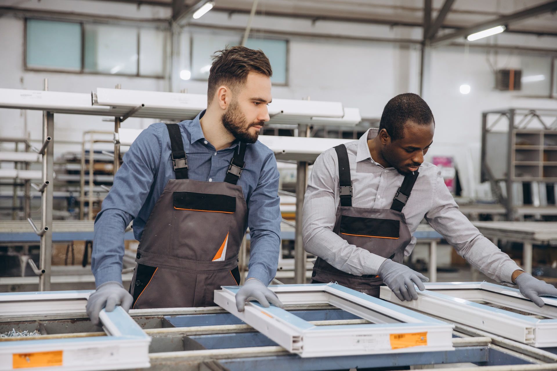 Two workers in overalls inspecting window frames in a factory.