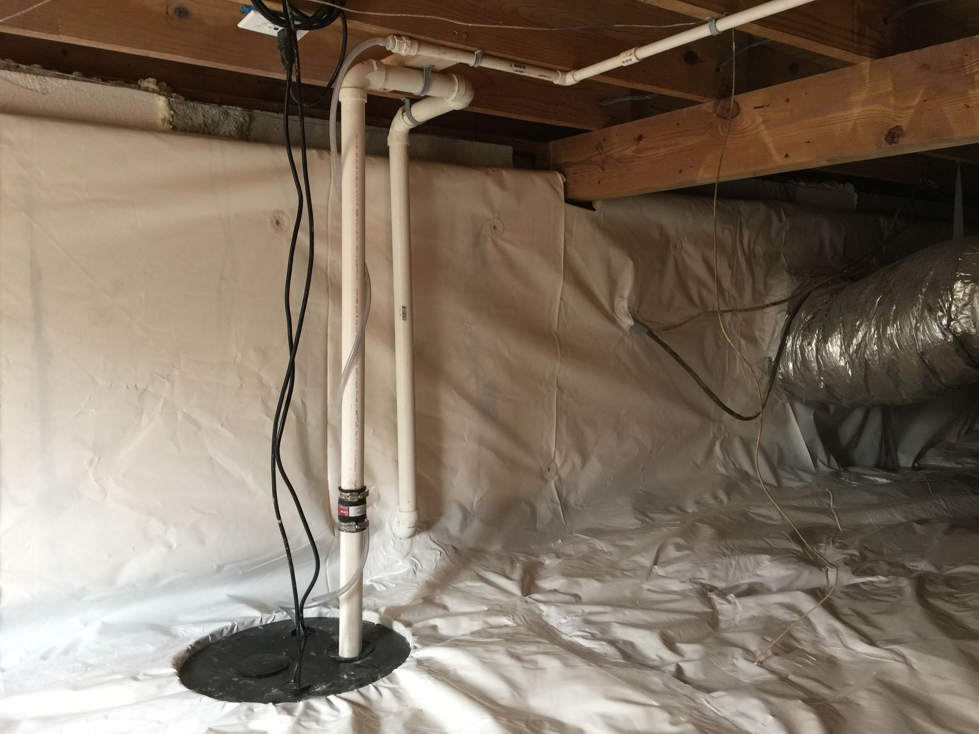 A basement with a sump pump and pipes in it.