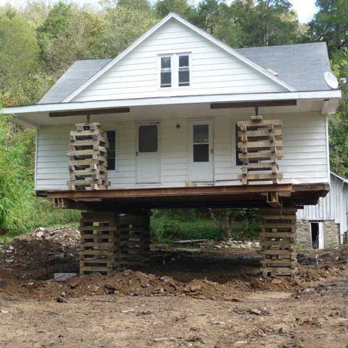 A white house is sitting on wooden stilts in a dirt field