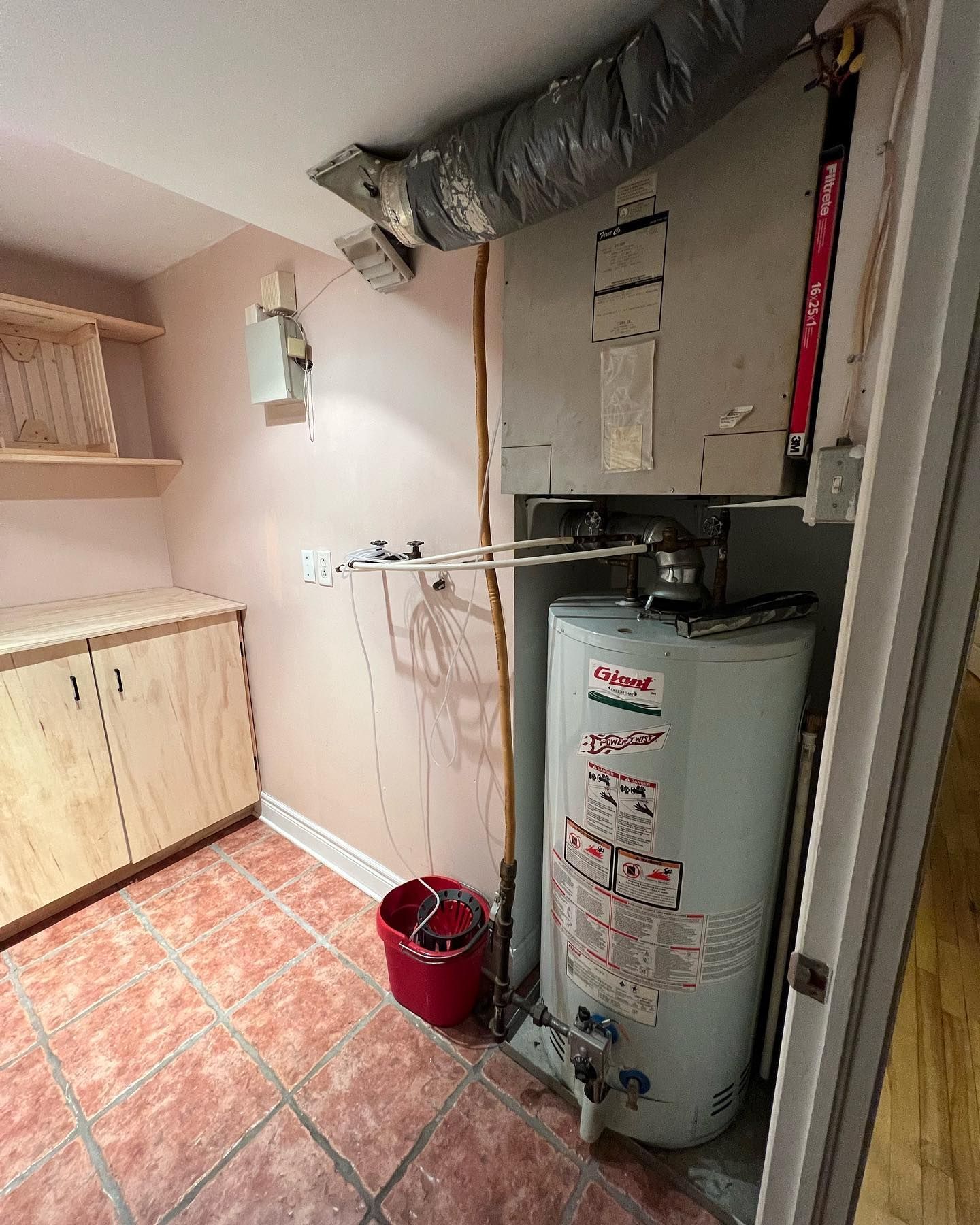 A room with a water heater and a red bucket.