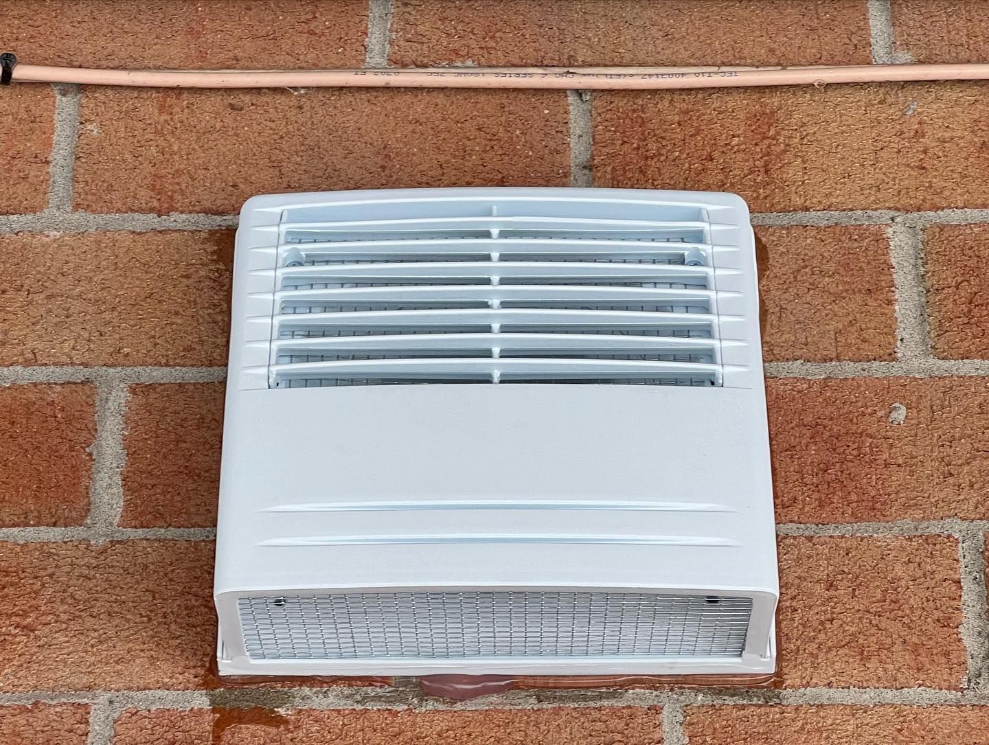 A white fan is mounted on a brick wall.