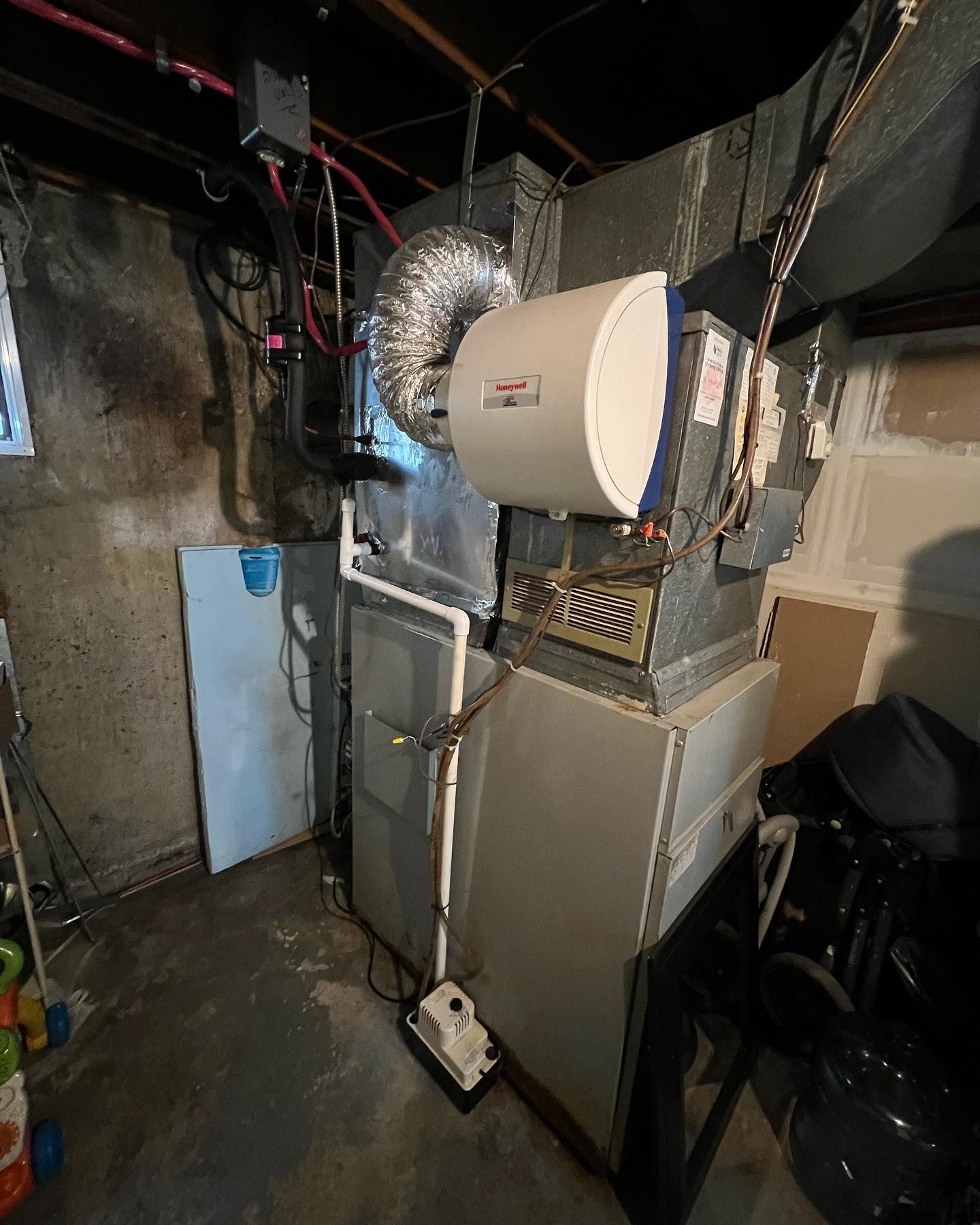 A boiler is sitting in a basement next to a refrigerator.